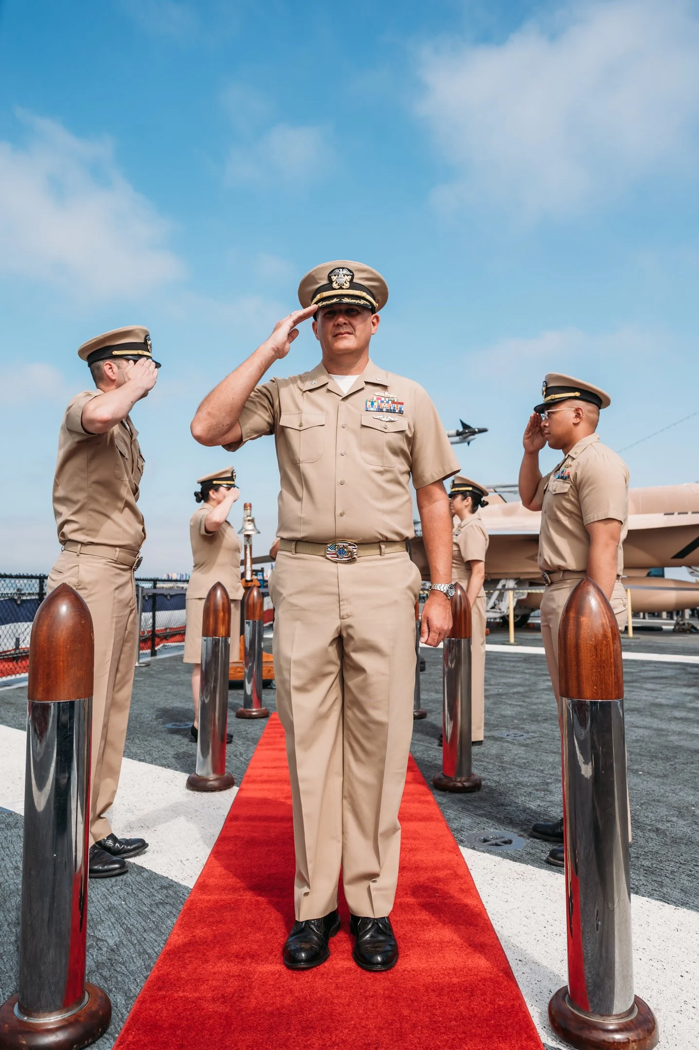 A group of military personnel standing on a red carpet on an aircraft carrier, saluting.  uss midway military retirement ceremony 