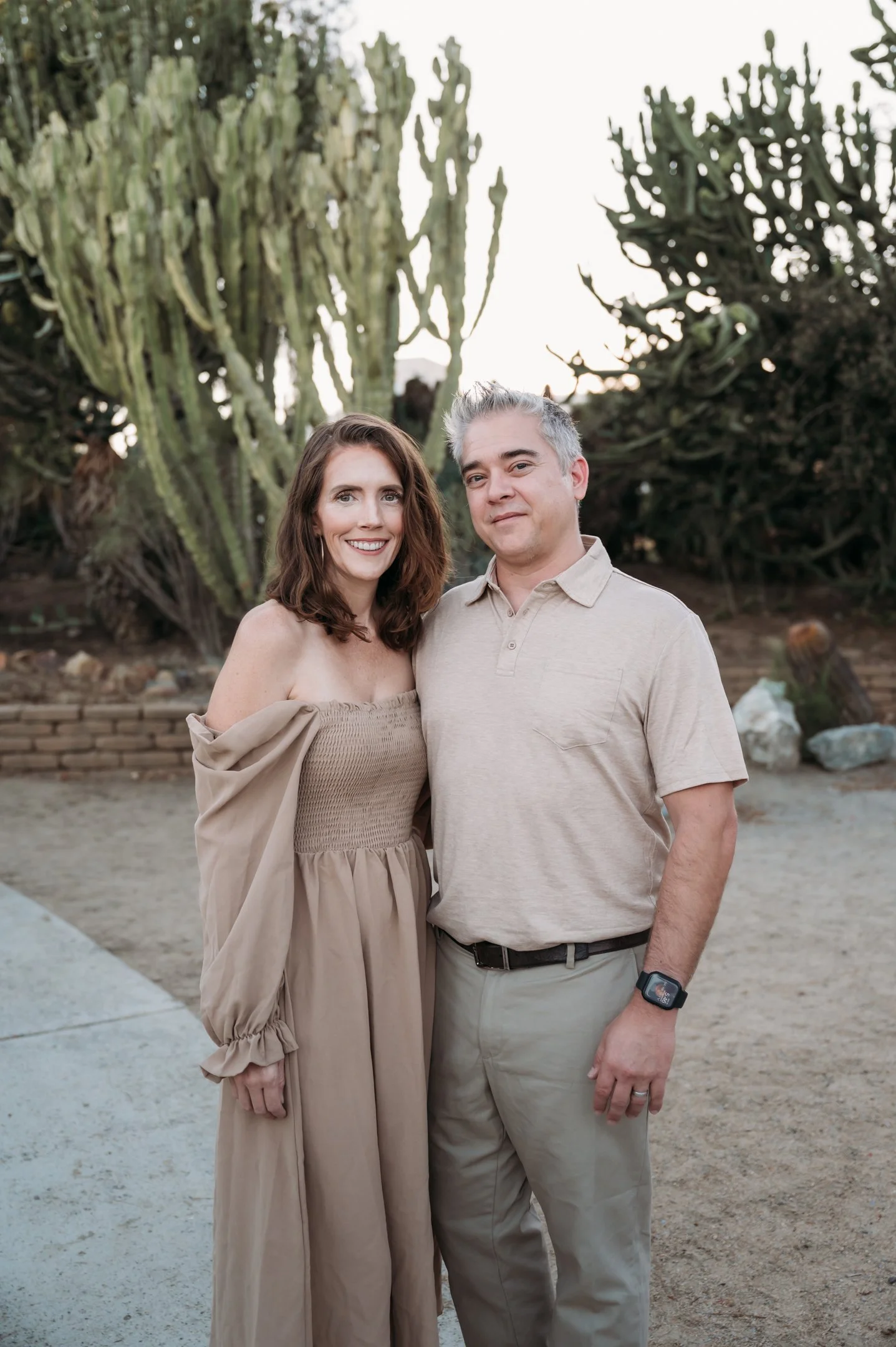 A smiling woman and man standing outdoors in front of cactus plants during sunset. Alisha Mowry Photography Military, Brand, and Portrait Photographer San Diego CA