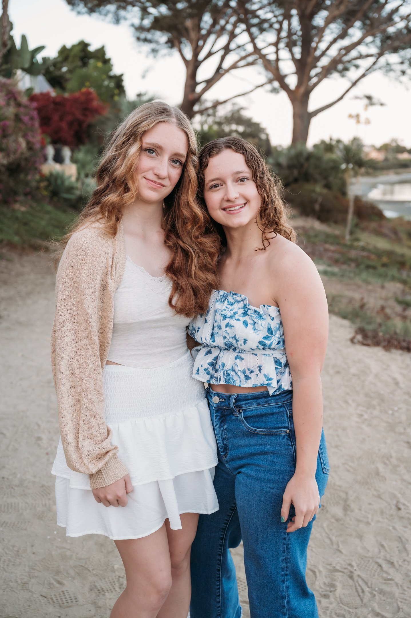Two young women standing outdoors on a sandy path with trees and bushes in the background, smiling at the camera. Alisha Mowry Photography Military, Brand, and Portrait Photographer San Diego CA