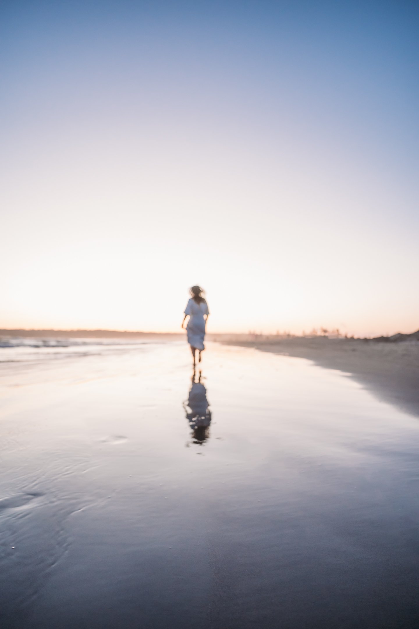 A person walking on the beach at sunset or sunrise with their reflection in wet sand. Alisha Mowry Photography Military, Brand, and Portrait Photographer San Diego CA