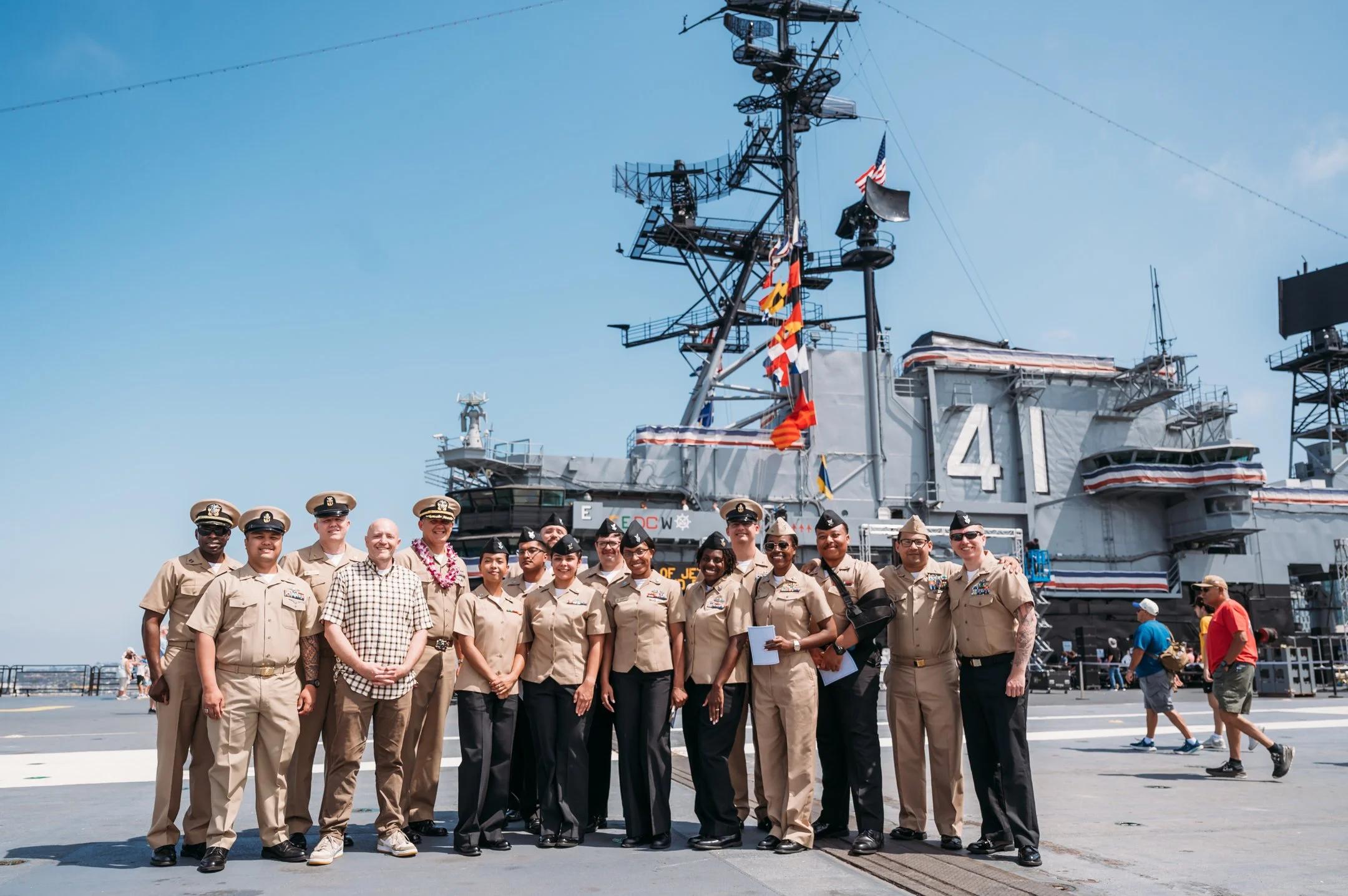 Group of US Navy personnel standing on an aircraft carrier deck with aircraft carrier ship in the background. uss midway military retirement ceremony 