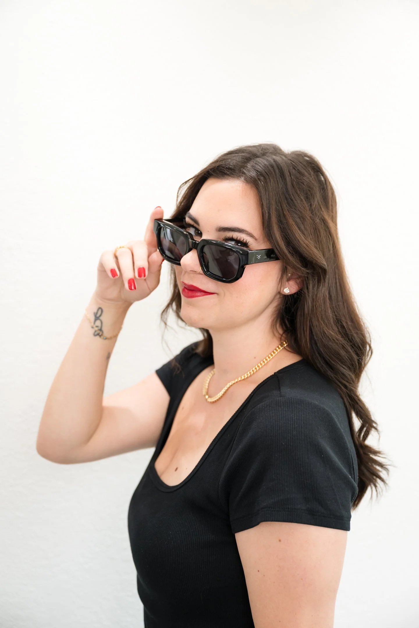A woman with shoulder-length brown hair, red lipstick, and red nail polish wears black sunglasses, a black t-shirt, a gold chain necklace,Alisha Mowry Photography Military, Brand, and Portrait Photographer San Diego CA