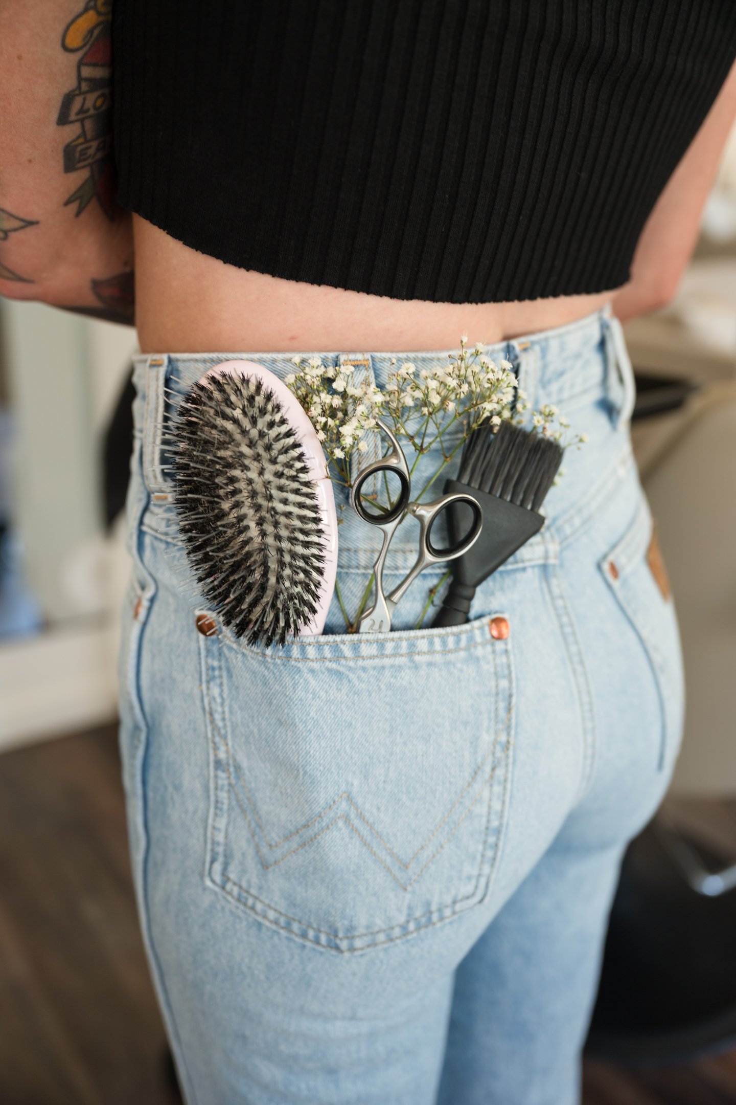 Close-up of a person wearing light blue jeans with a black top, with hairstyling tools and flowers in the back pocket of the jeans. Alisha Mowry Photography Military, Brand, and Portrait Photographer San Diego CA