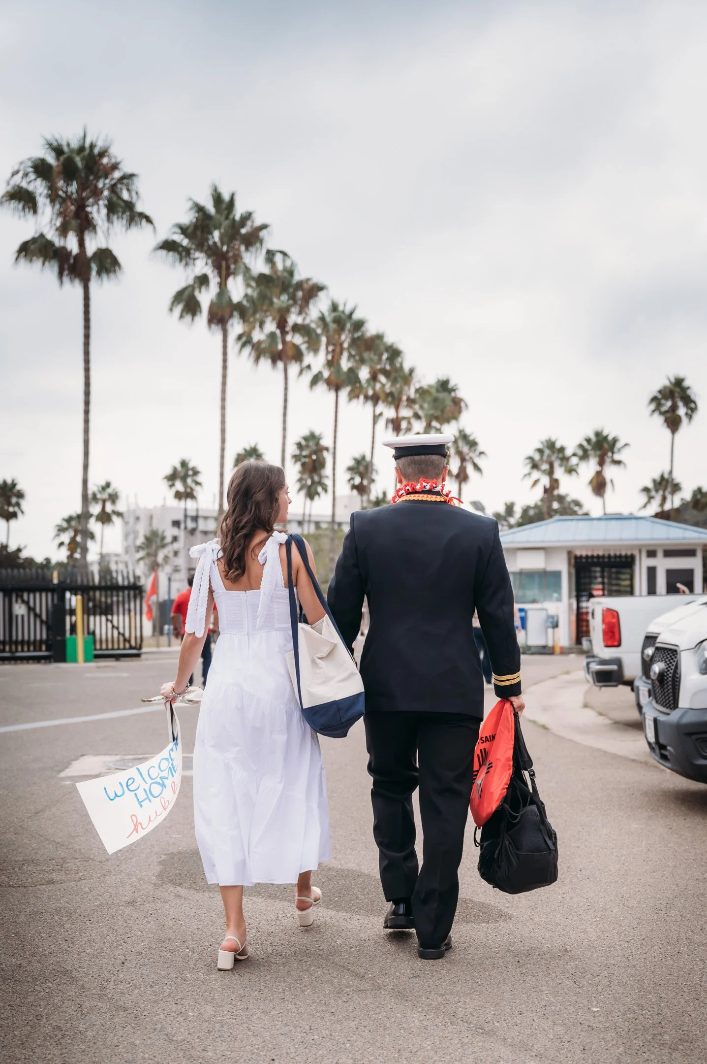 A woman and a man in a navy uniform walking away with palm trees in the background  Alisha Mowry Photography Military Photographer San Diego