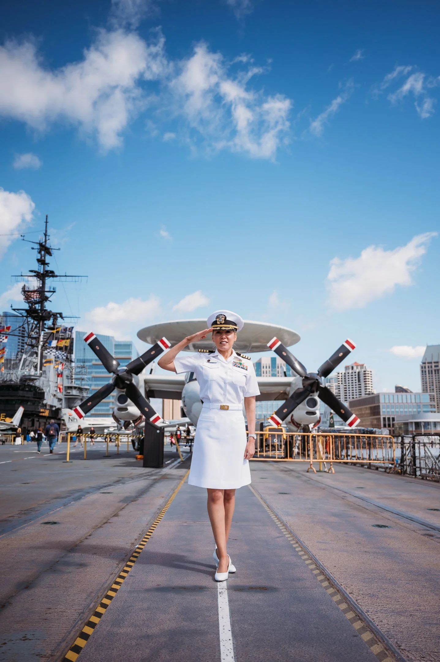 A woman in a white military uniform salutes in front of a large military aircraft on a navy ship's deck. Alisha Mowry Photography Military Photographer San Diego