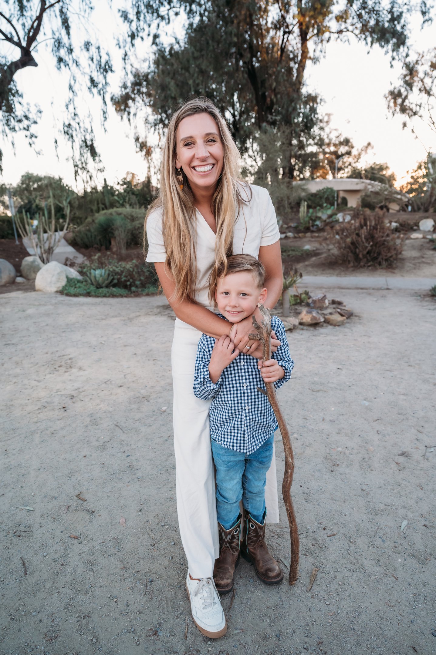 A smiling woman with long blonde hair stands behind a young boy with short hair, holding his arms. Alisha Mowry Photography Military, Brand, and Portrait Photographer San Diego CA