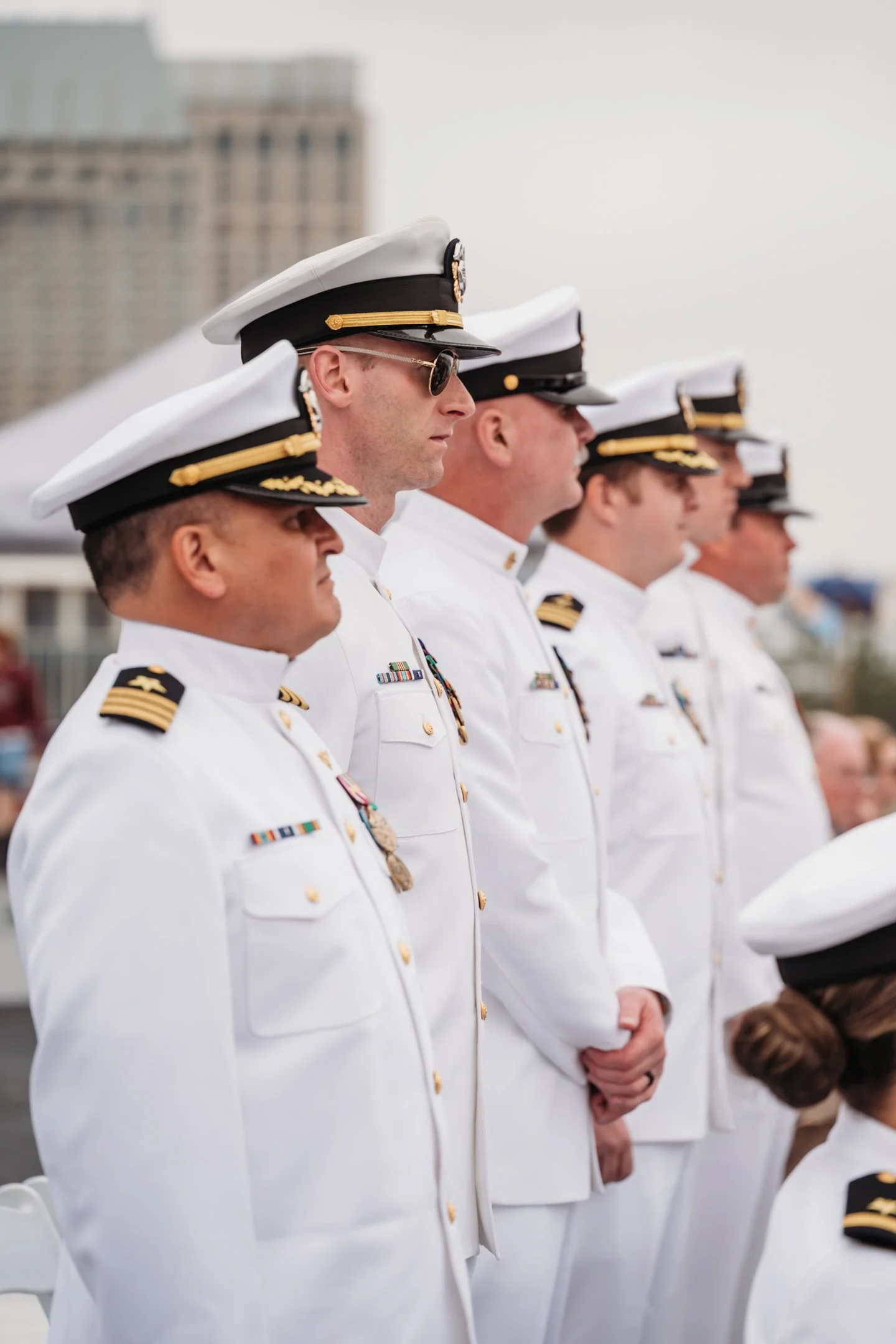 Line of Navy officers in white uniforms and caps at an outdoor ceremony, with city buildings in the background.  uss midway military retirement ceremony 