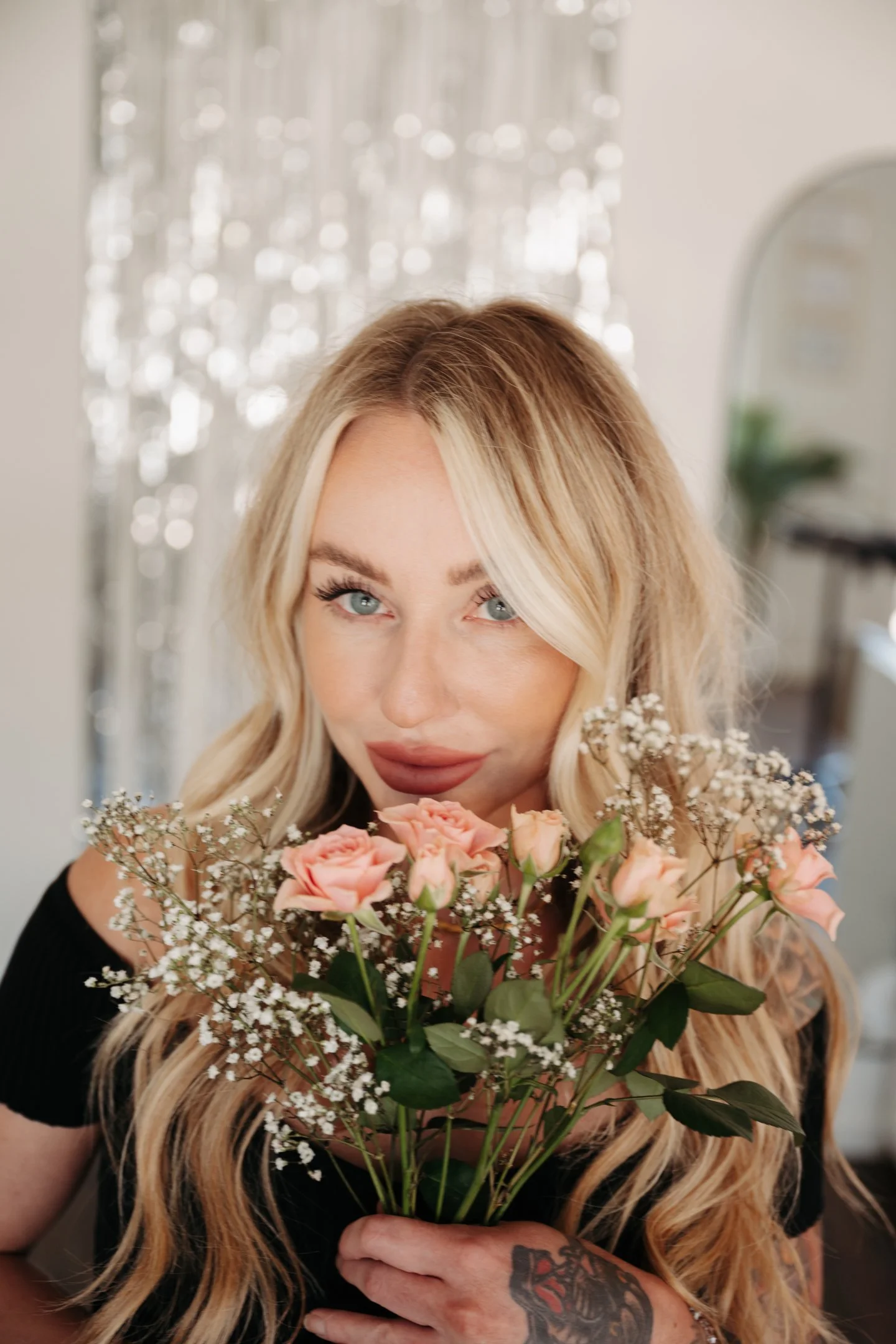 Woman with blonde hair holding a bouquet of pink roses and baby's breath, smiling at the camera indoors. Alisha Mowry Photography Military, Brand, and Portrait Photographer San Diego CA