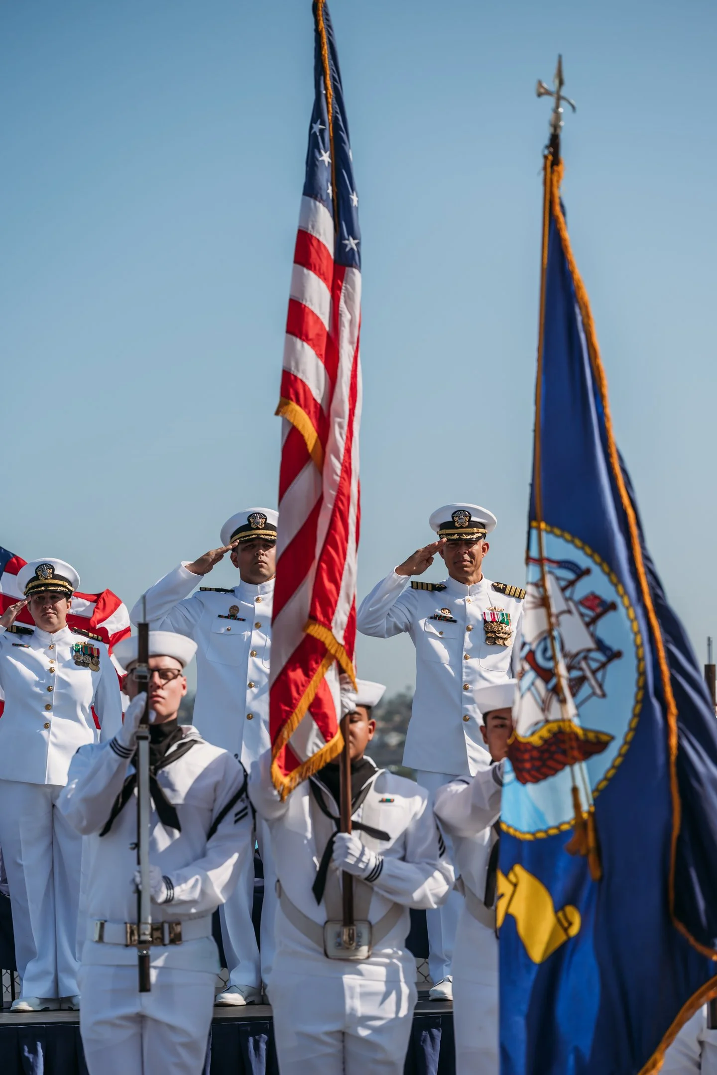 U.S. Navy sailors standing and saluting during a ceremonial event with flags in the foreground. Alisha Mowry Photography Military Photographer San Diego