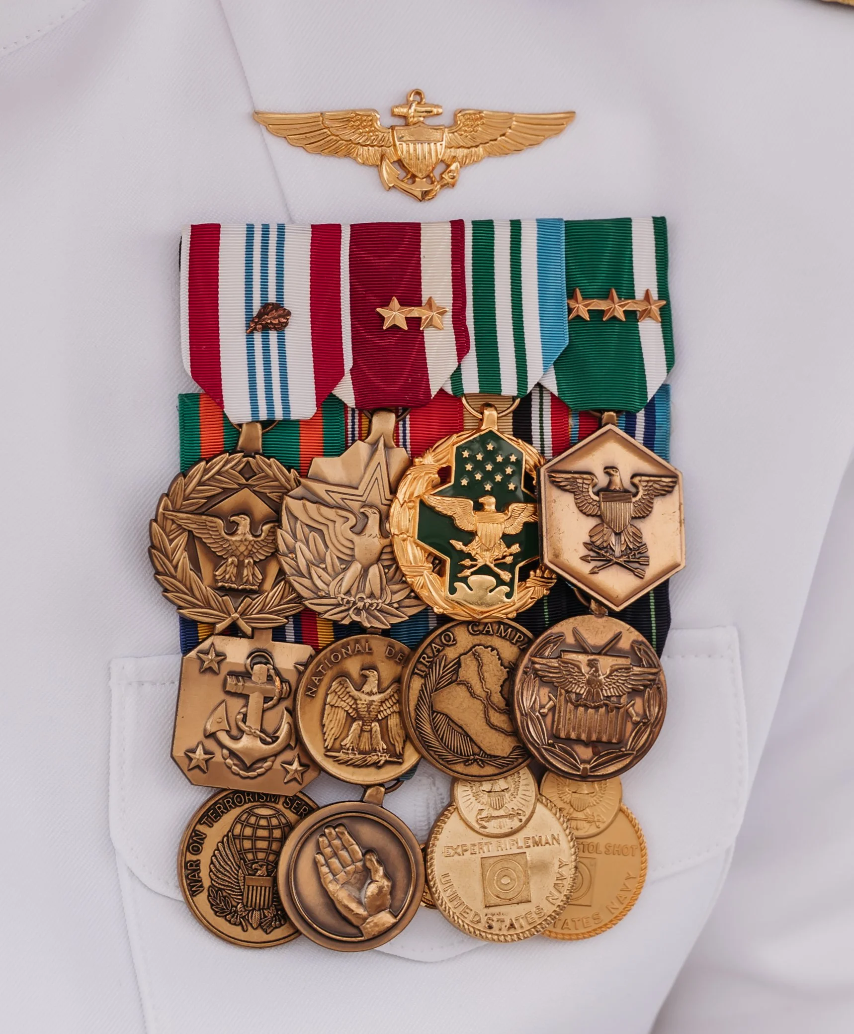 A collection of military medals and ribbons on a white uniform pocket, with a gold pin above.
