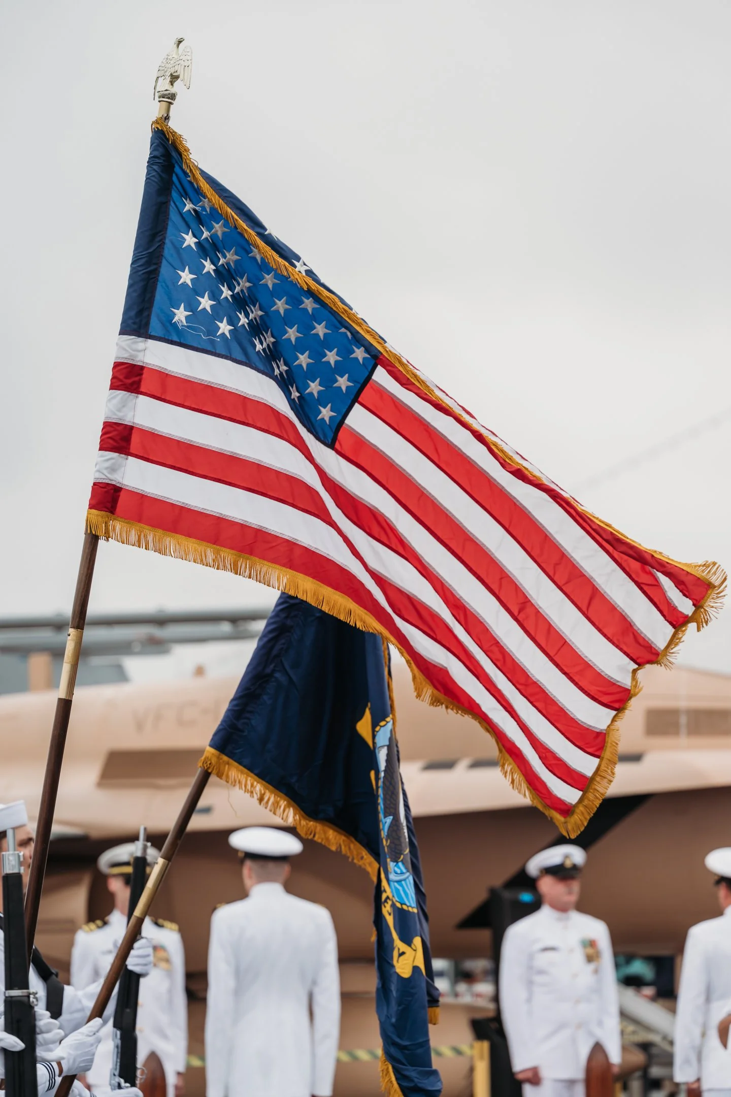 U.S. flag waving in front of servicemen in white military uniforms during a military retirement ceremony on the USS Midway in San Diego CA