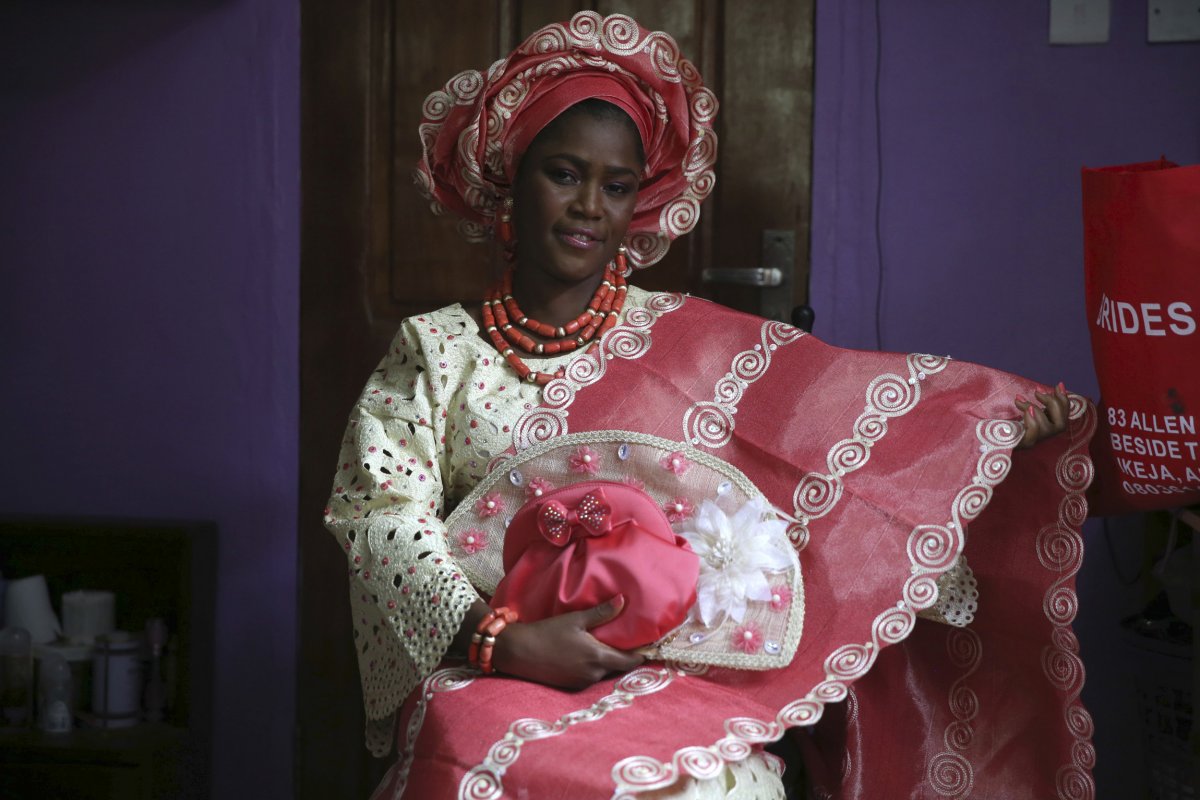 This beautiful Nigerian bride is traditionally dressed in a brightly colored lace blouse and patterned kaftan. She has on coral beads and a headdress to bring the wedding attire together. The bride can decide on what color she would like her blouse and kaftan to be and matches her beads and headdress accordingly. 