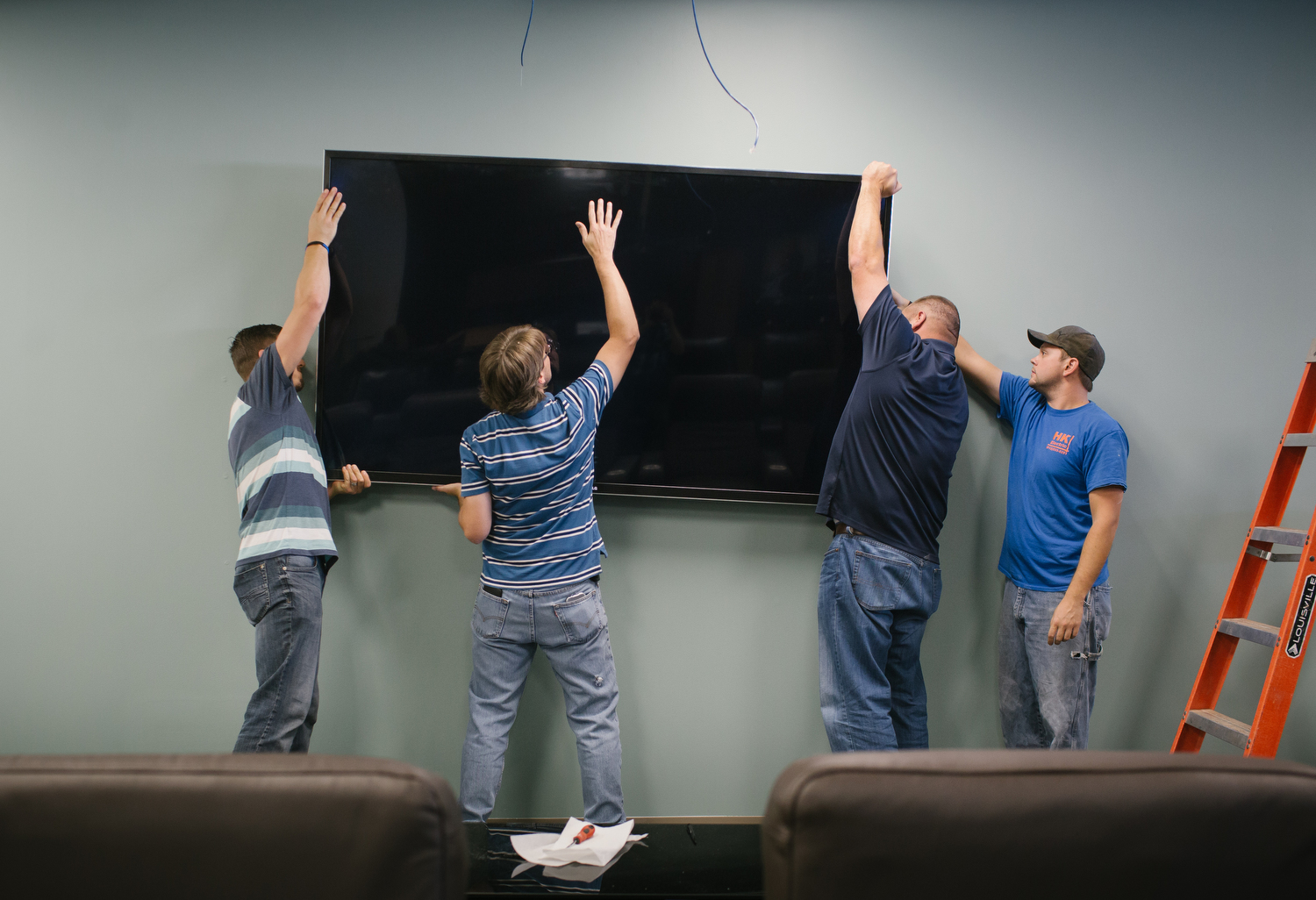 PILR TECH employees, from left to right, Ryan Meredith, Michael Black and Michael Cory and Matthew Williams, with HK Electric, install an 85 inch tv at their office in Joplin, Mo. Photo by Brad Zweerink