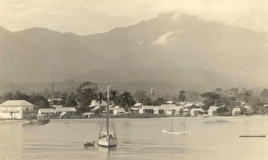 Partial view of La Ceiba waterfront in the 1910s. The sender of this real photo postcard, possibly an American missionary, describes the white building behind the boat's mast as "our church" and the large building at the left as the barracks and prison.The wireless station and tower to the right of the water tower belonged to "an American banana company", most likely the company that became the Standard Fruit Co. and whose operations were headquartered in La Ceiba. Unknown, c. 1915 - Public Domain
