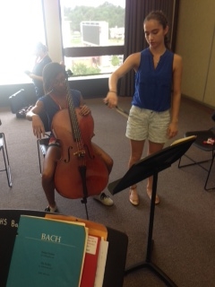 After her lesson, a student (standing) teaches a basoonist (seated), the basics of Cello. U of A Camp 2014