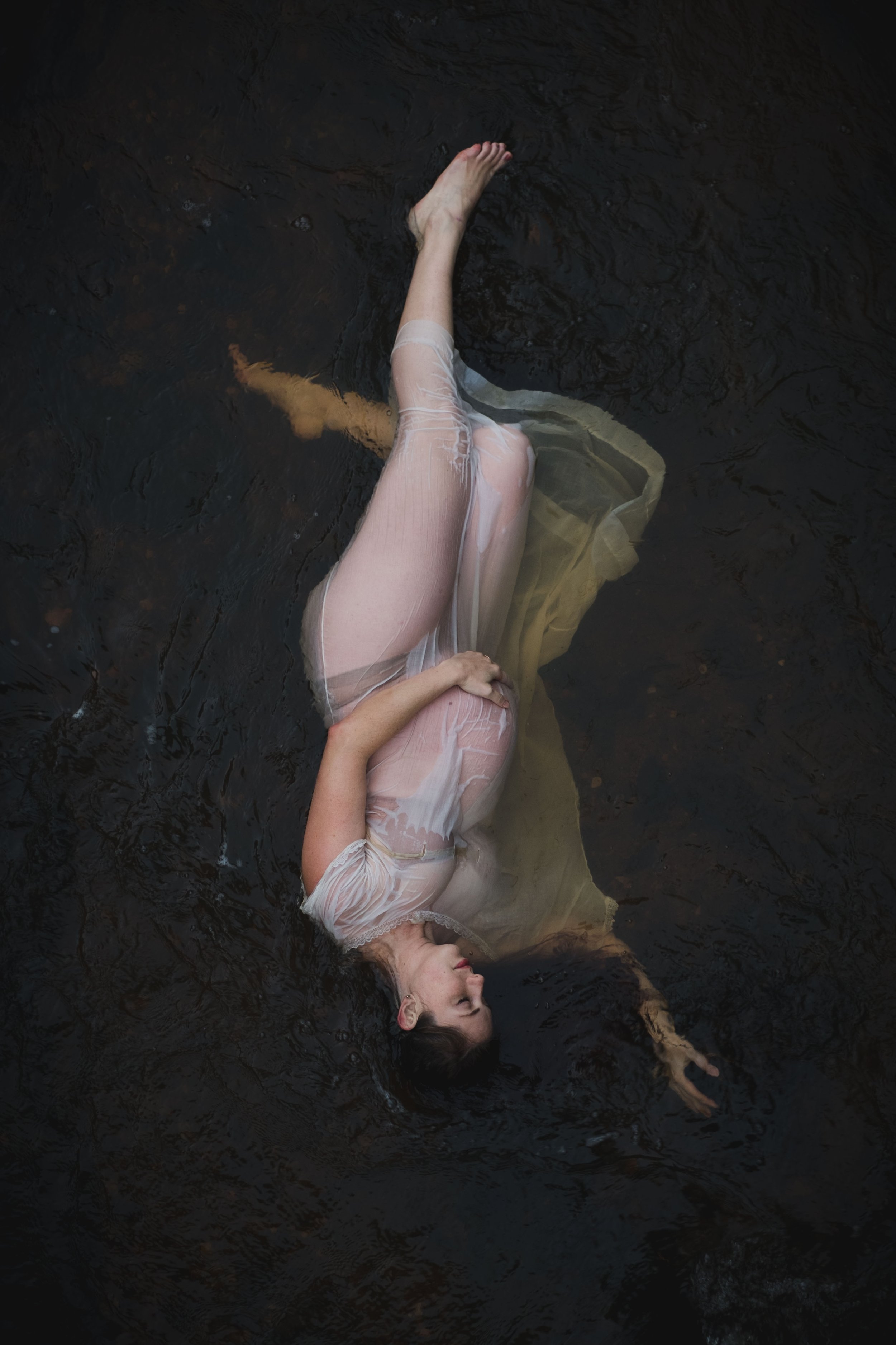 maternity photoshoot of pregnant woman floating in river in a sheer antique dress