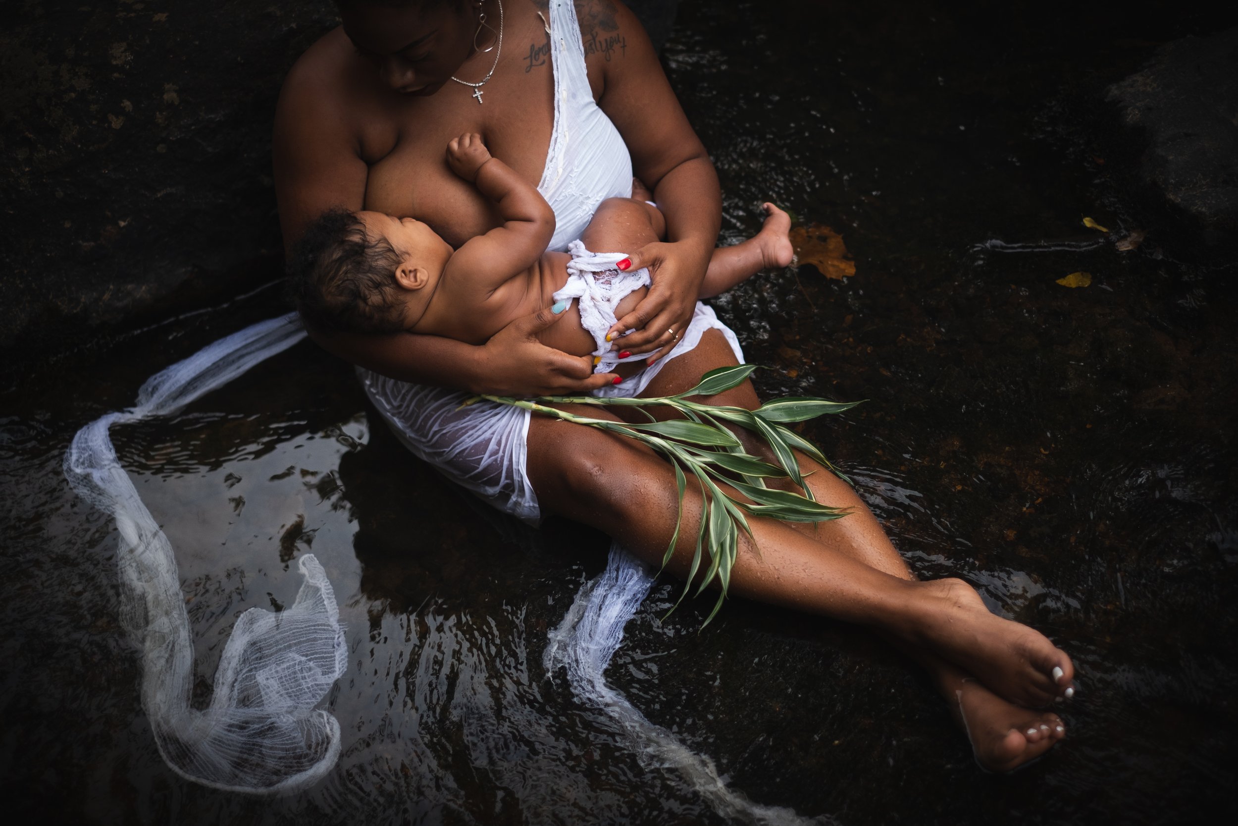 black mom breastfeeding her baby in a river