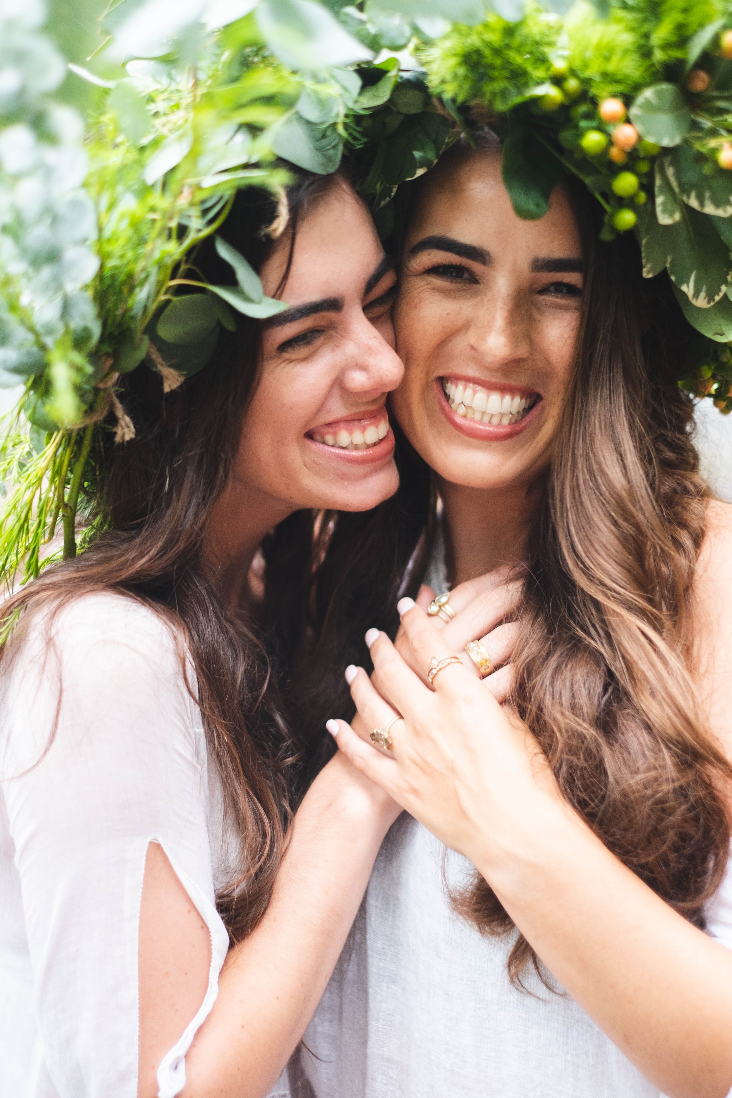 two sisters wearing nature crowns and white dresses laughing feeling joy and wearing Jennifer Dawes Jewelry