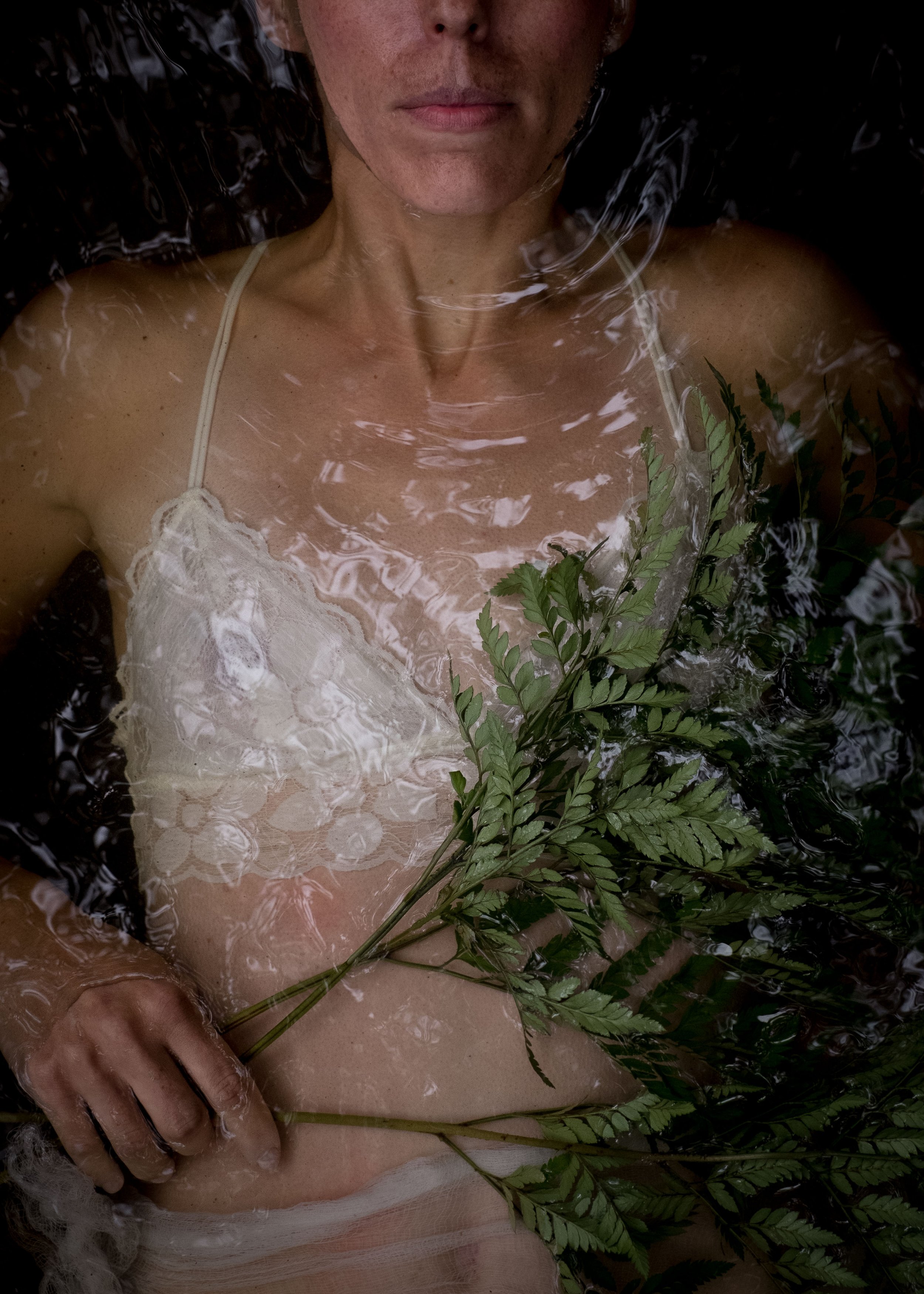 woman with freckles wearing lacy sheer bralette in river water holding greenery