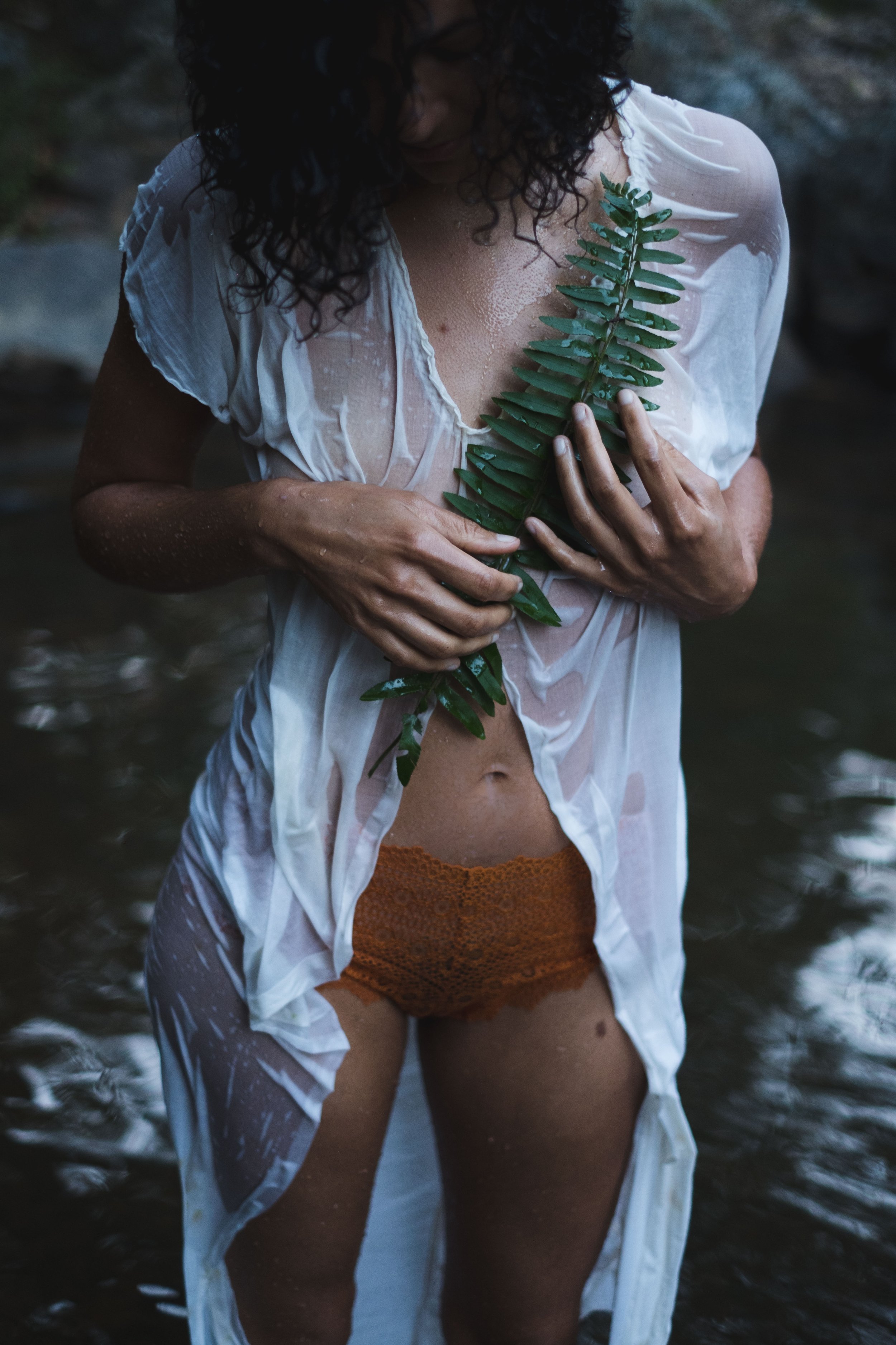 woman stading in a river wearing ripped sheer antique lacy underware dress holding fern 