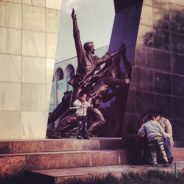 A family sits by a memorial commemorating the 2010 Revolution that overthrew Kurmanbek Bakiyev. This revolution was preceded by the Tulip Revolution in 2005, during which Askar Akayev was forced from power. (at Bishkek, Kyrgyzstan)