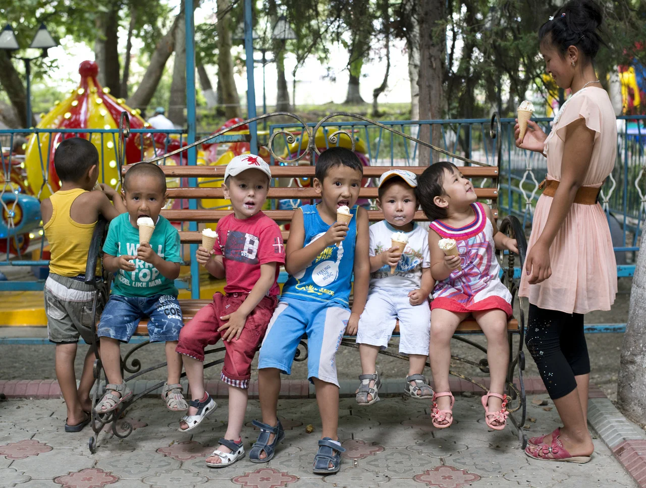 A babysitter watches over a group of kids as they eat ice cream in one of the several permanent parks established during the Soviet Era in Osh, Kyrgyzstan. The permanent amusement park is about 800m long and features bumper cars, cotton candy, bb gu…