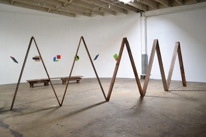 installation view of "Lean, 2", wooden sculpture in the foreground. Tempera and gouache paintings on a curved wall behind the sculpture. 2011