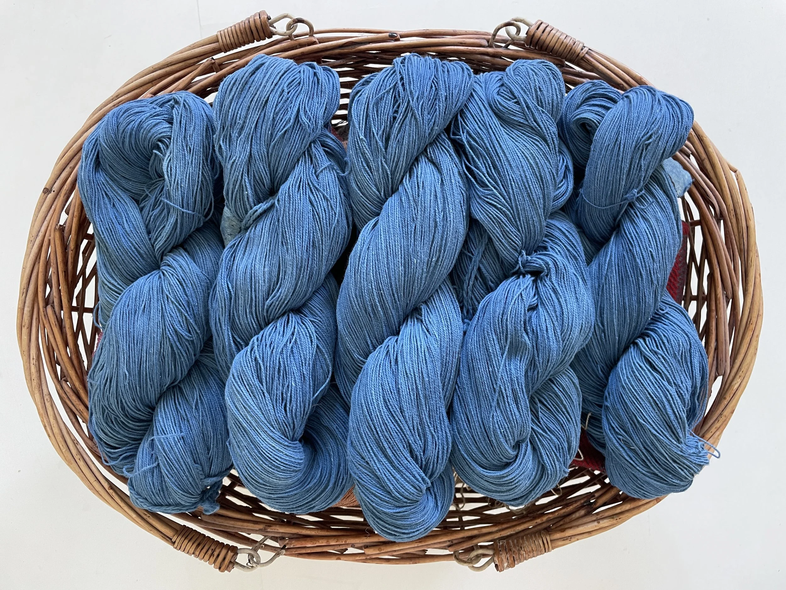 Several skeins of indigo dyed blue yarn in a wicker basket.