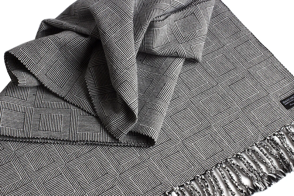 A black and white patterned scarf with fringed edges, folded and draped to show its geometric design.
