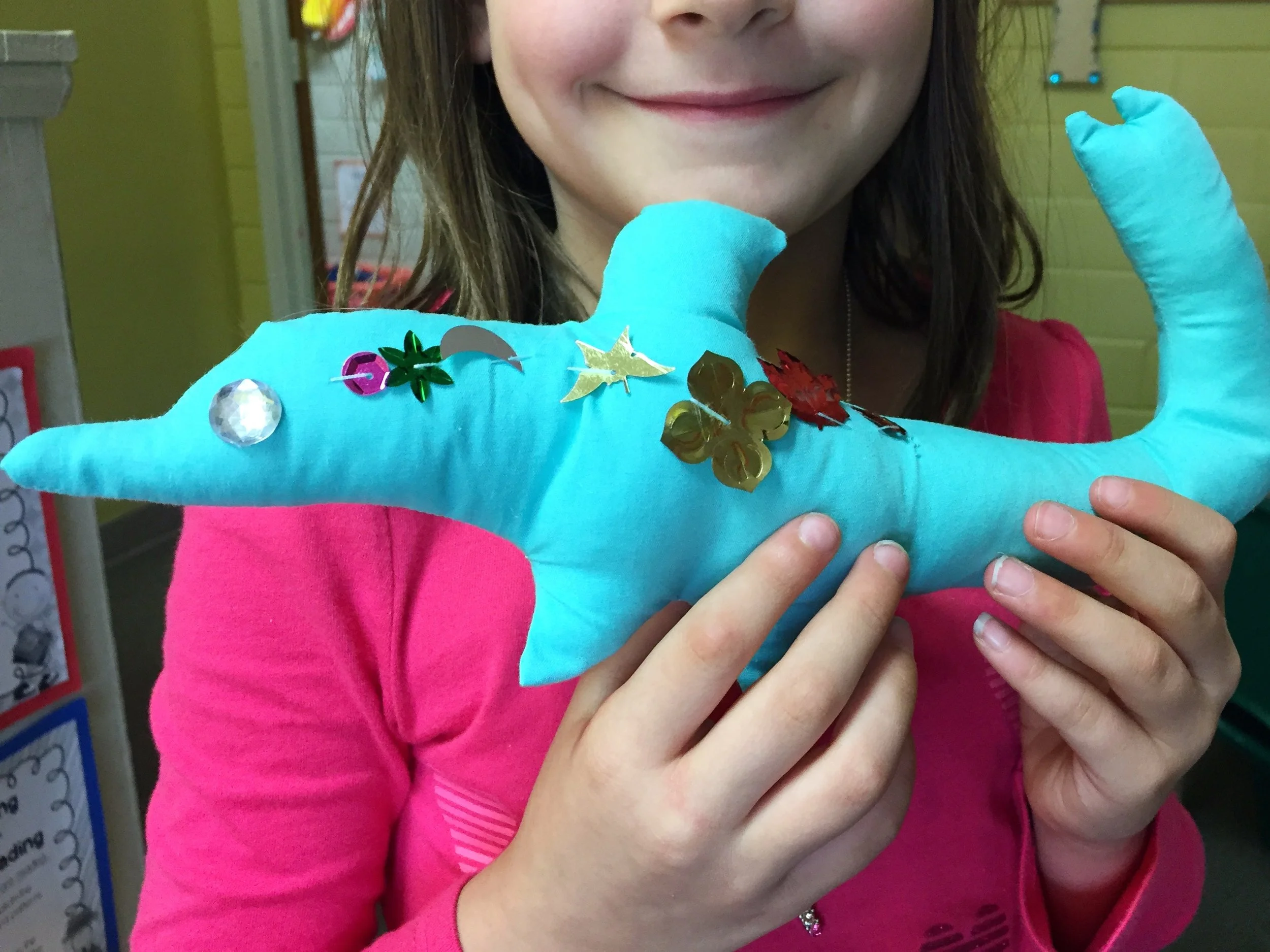 A third grader holding up the hand sewing project she made from a small group sewing lesson.