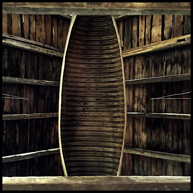 Canvas-hulled canoe at rest on barn beams