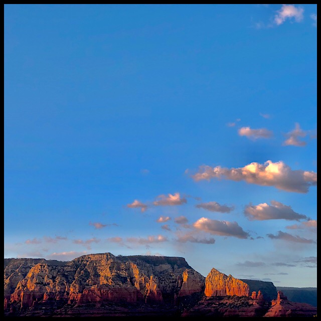 Clouds arpeggiating over red cliffs in setting sun