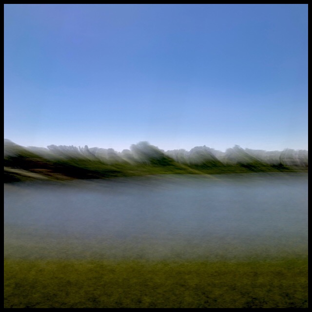 Tree-lined riverbank with reflected sky, from train at speed, slow shutter