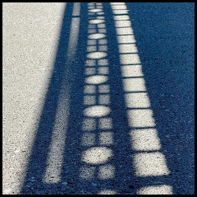 Railing shadow on paved walkway