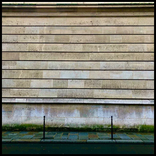 Wall of silent staves above rain-bright flagstone sidewalk