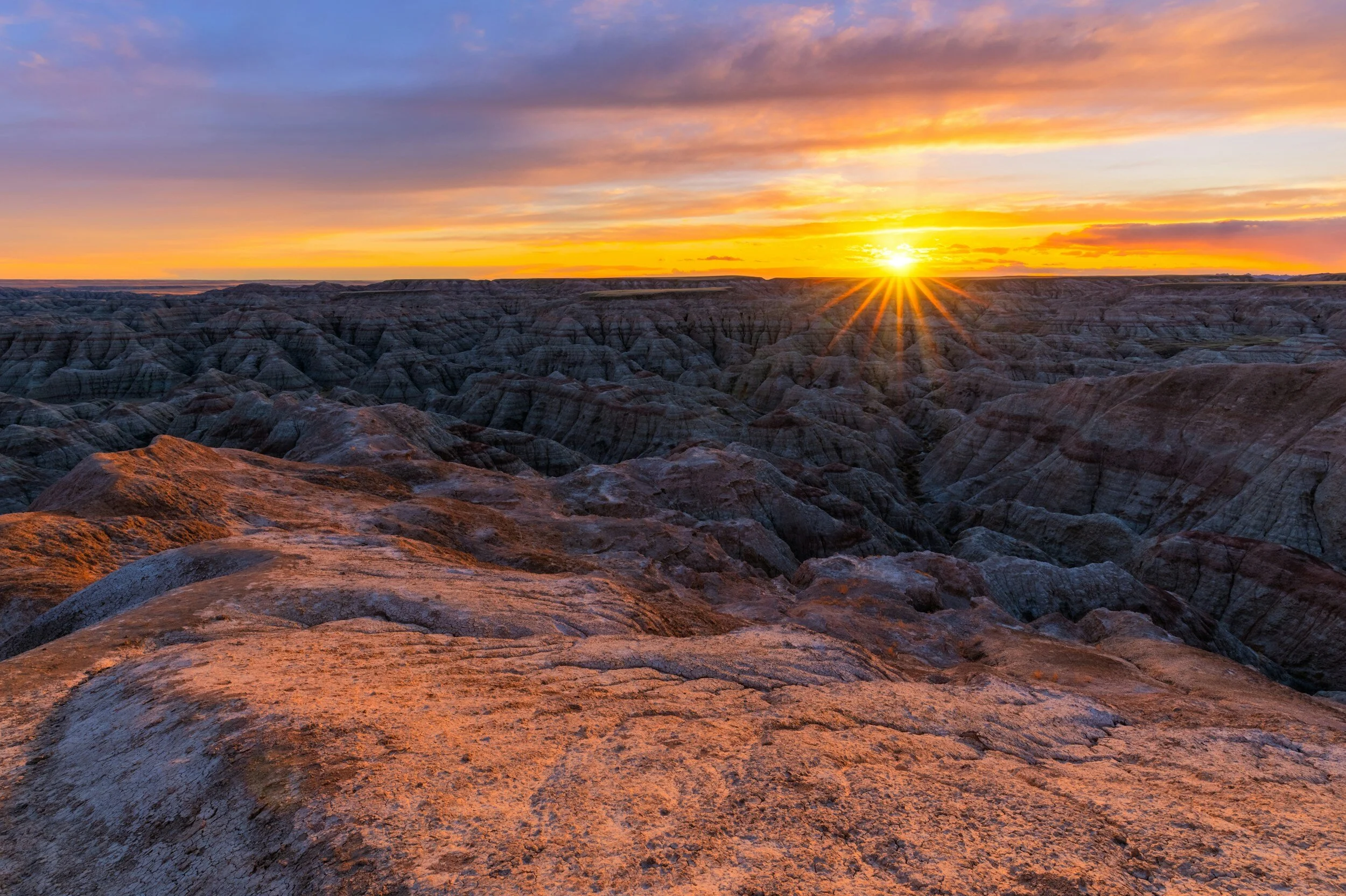 A sun hovers over the horizon of crested buttes in badlands national park