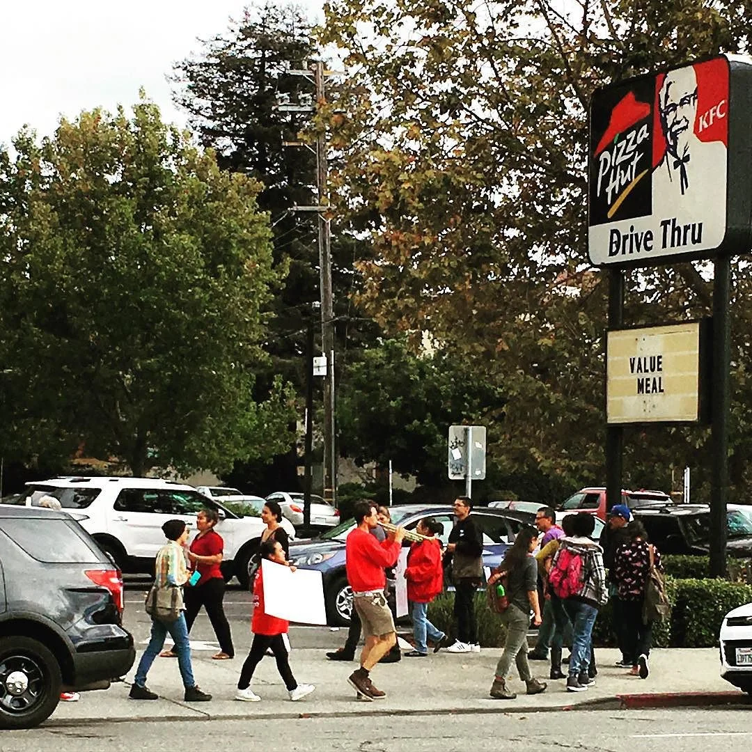 About 20 people chant "sí se puede" outside combination Pizza Hut & KFC. Cop cars present: 5. #2milesoftelegraph