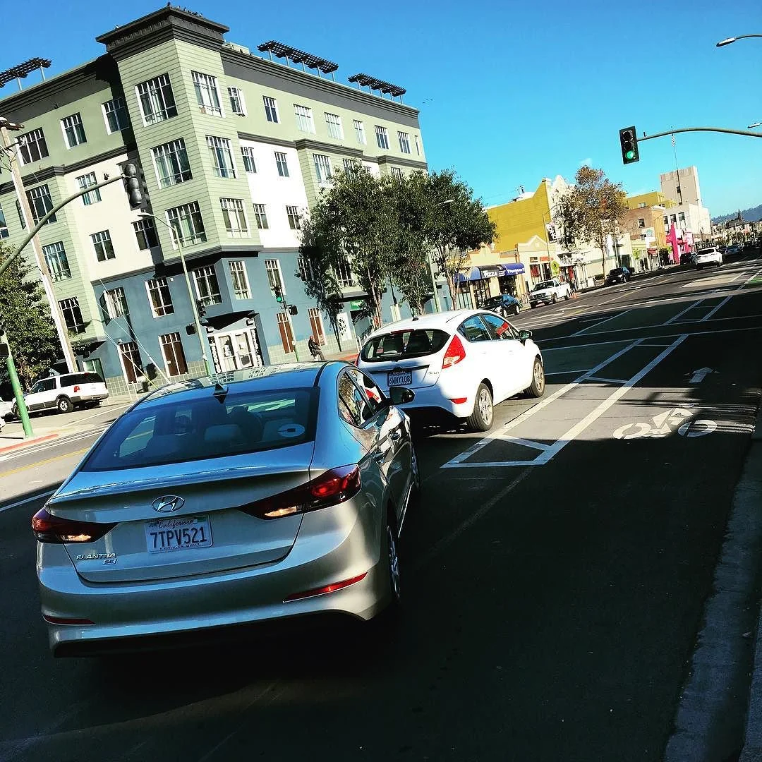 Rear car doesn't realize front car is parked in new parking spot meant to accommodate dedicated bike lane. After honking several times, rear car passes parked car on the right, inside the bike lane. #oakland #userstudy #2milesoftelegraph