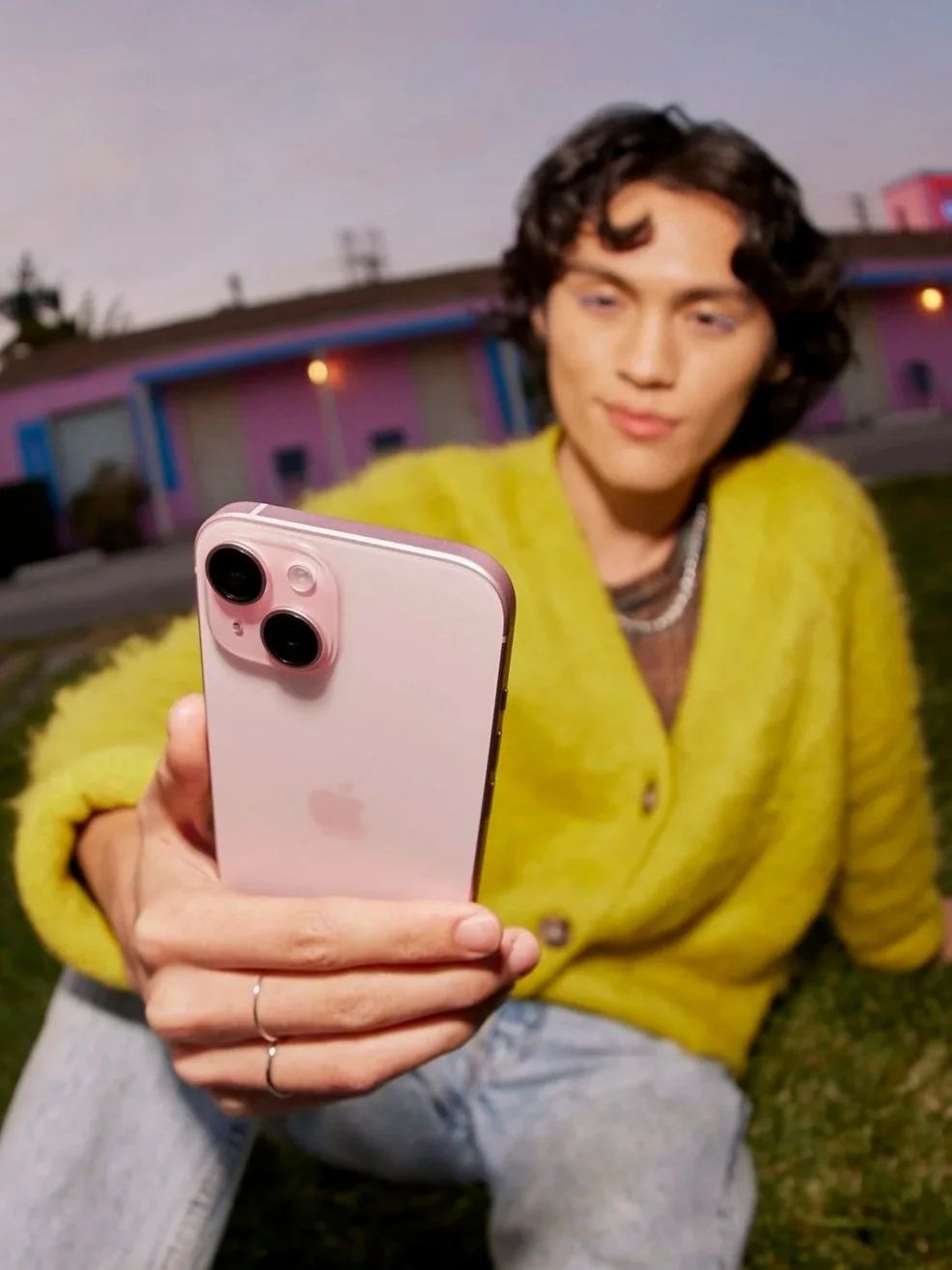 Person with curly hair wearing a green fuzzy cardigan taking a selfie with an iPhone outdoors