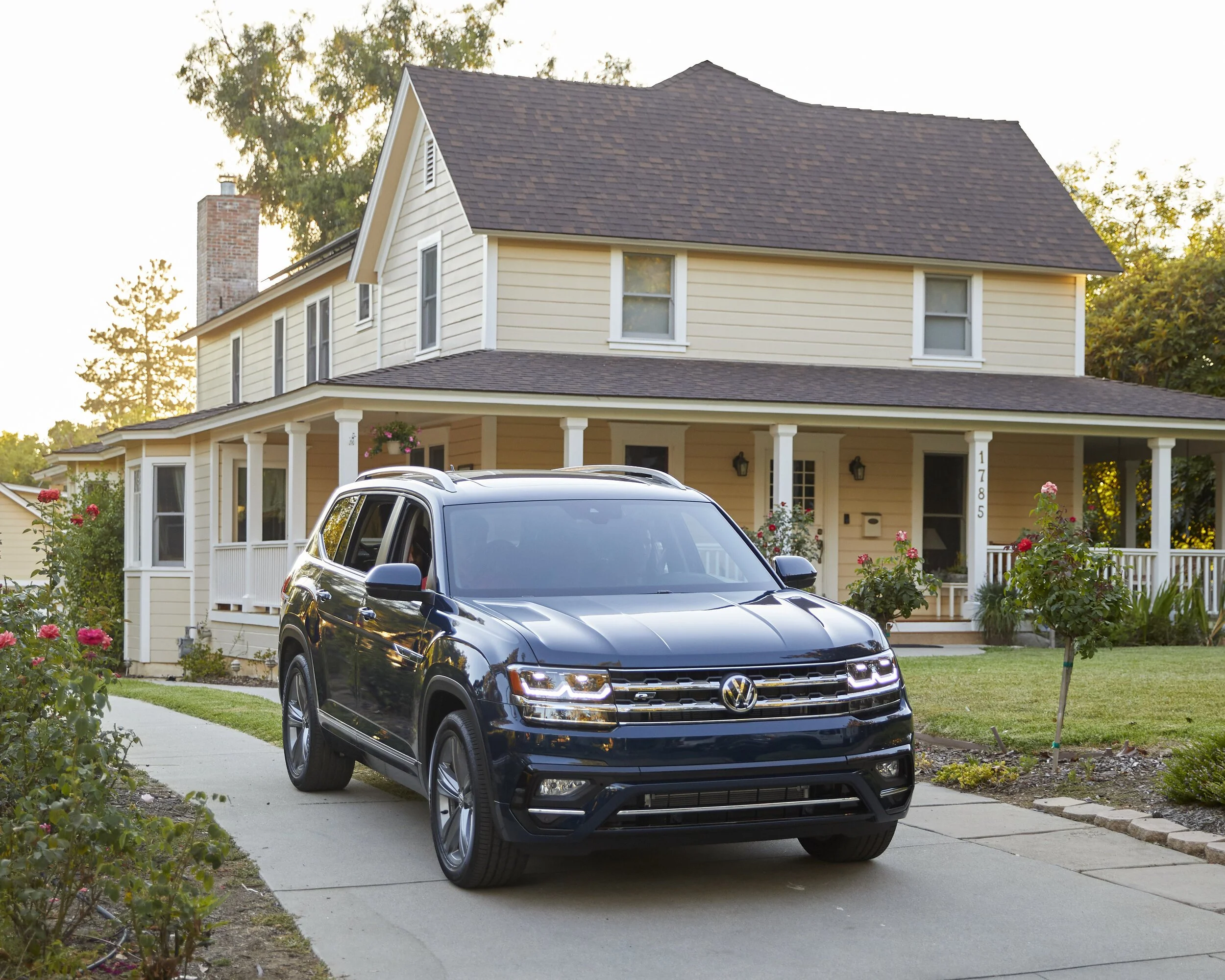Black Volkswagen SUV parked in front of a two-story house with a porch, surrounded by a well-maintained lawn and garden with blooming roses.