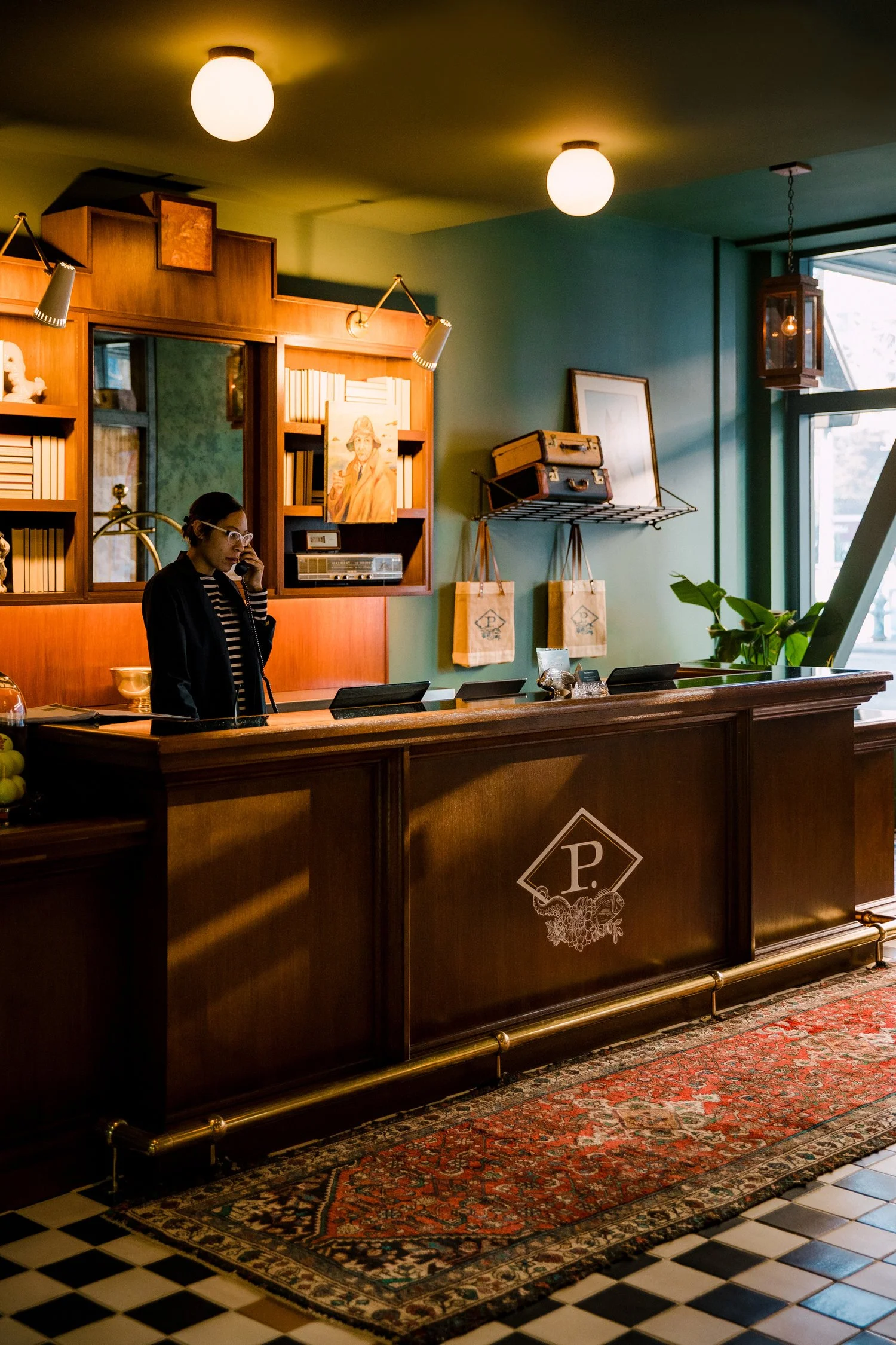 Reception desk with a woman talking on phone, in a cozy, vintage-style interior with books, artwork, and decorative items.