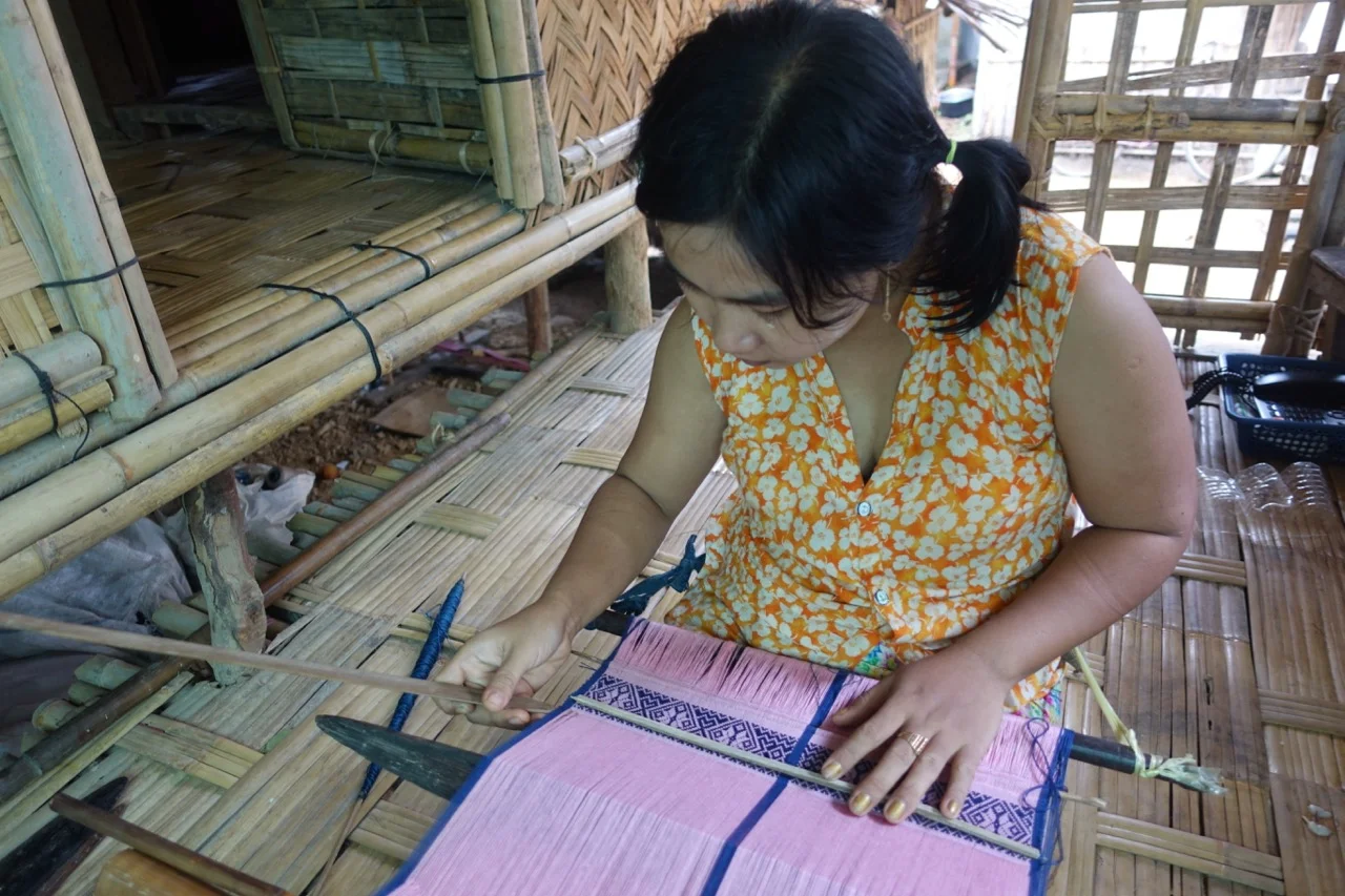 Pin Ei Nwe , is one of the busiest women in Myothit! She is the mother of 3 young children and her family has a community rice grinding business. Pin also runs a thread shop out of her home were she sells to all the weavers of Myothit, she also teaches weaving to people who want to learn, and has been designing a line of shoulder bags for Mro society which are super popular! And she has now taken on the supervisor role for all the weavers in the area.