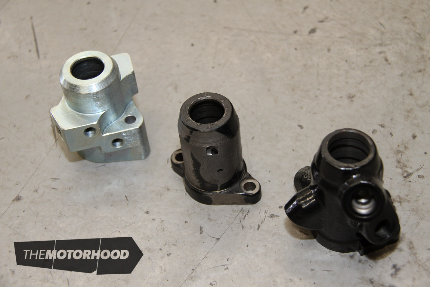 You can see the progress here as the original valve body (right) was first machined down to fit into the narrow space required (centre), before a full custom item was produced (left), shifting the port positions for optimal hose position.