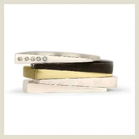 A stack of asymmetrical rings in sterling silver, black patina, gold, and mini diamonds.
