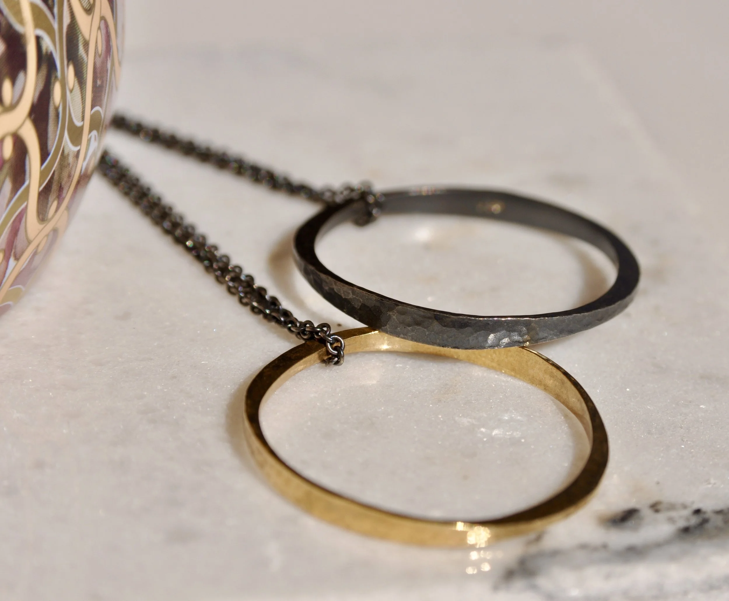 Angled close-up view highlighting the hand-hammered finish and contrast between the patinated sterling silver and gold rings.