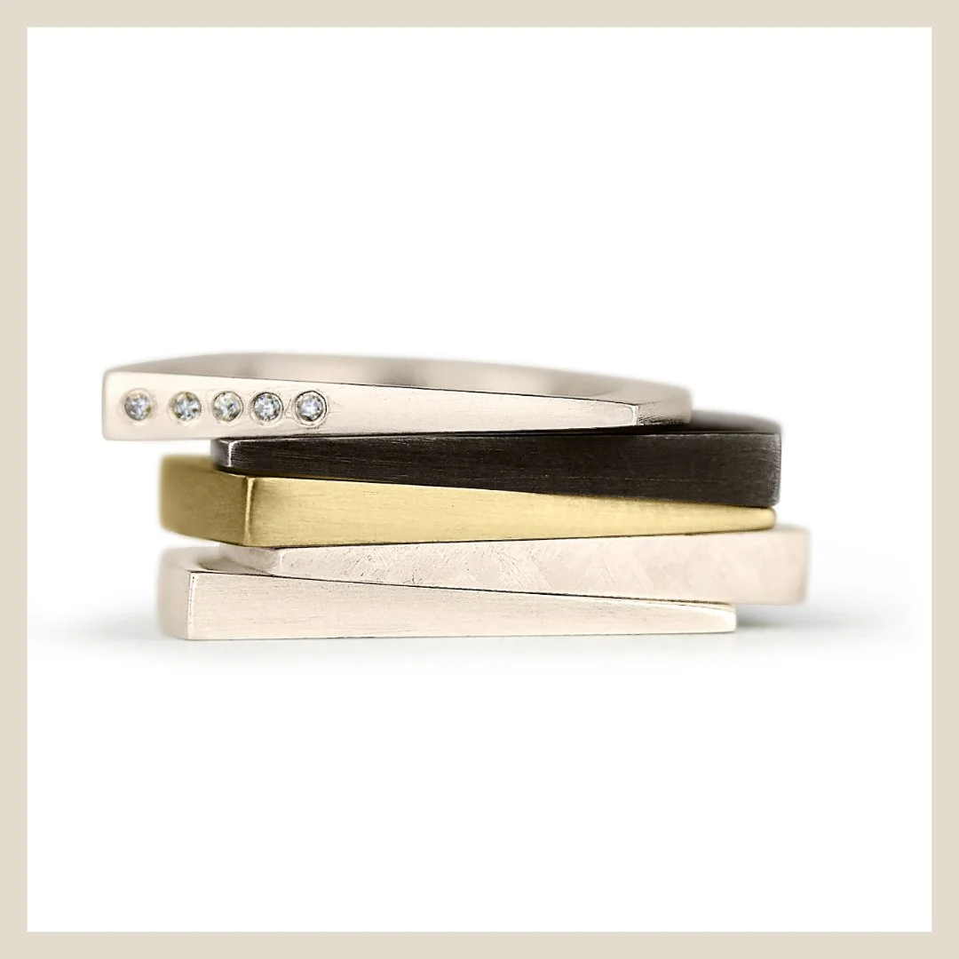 a stack of rings, one with a diamond, another black patina sterling silver, gold, brushed finish silver fine jewelry by eatmetal