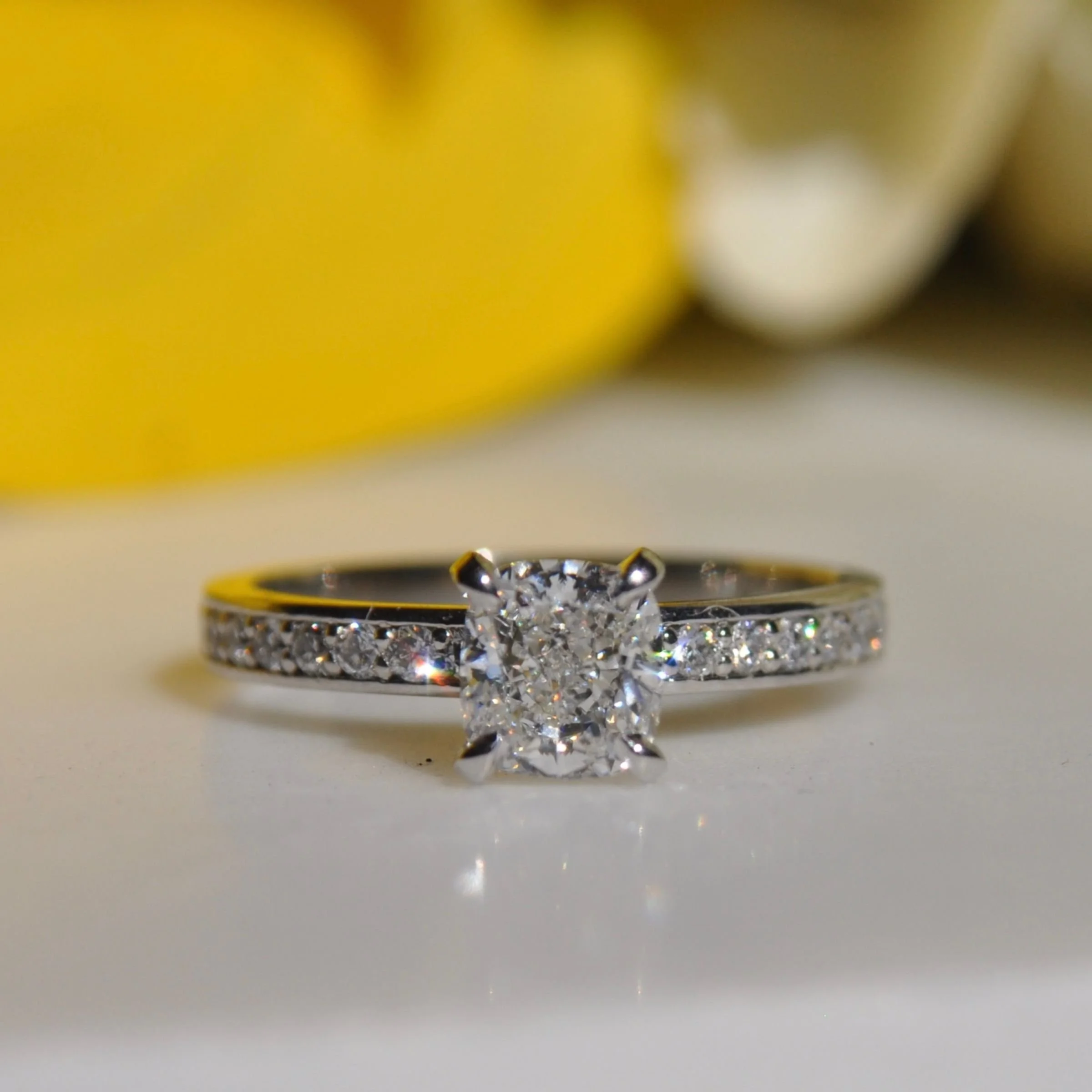 A contemporary diamond engagement ring featuring a brilliant cushion-cut center stone on a platinum pavé band with round accent diamonds.