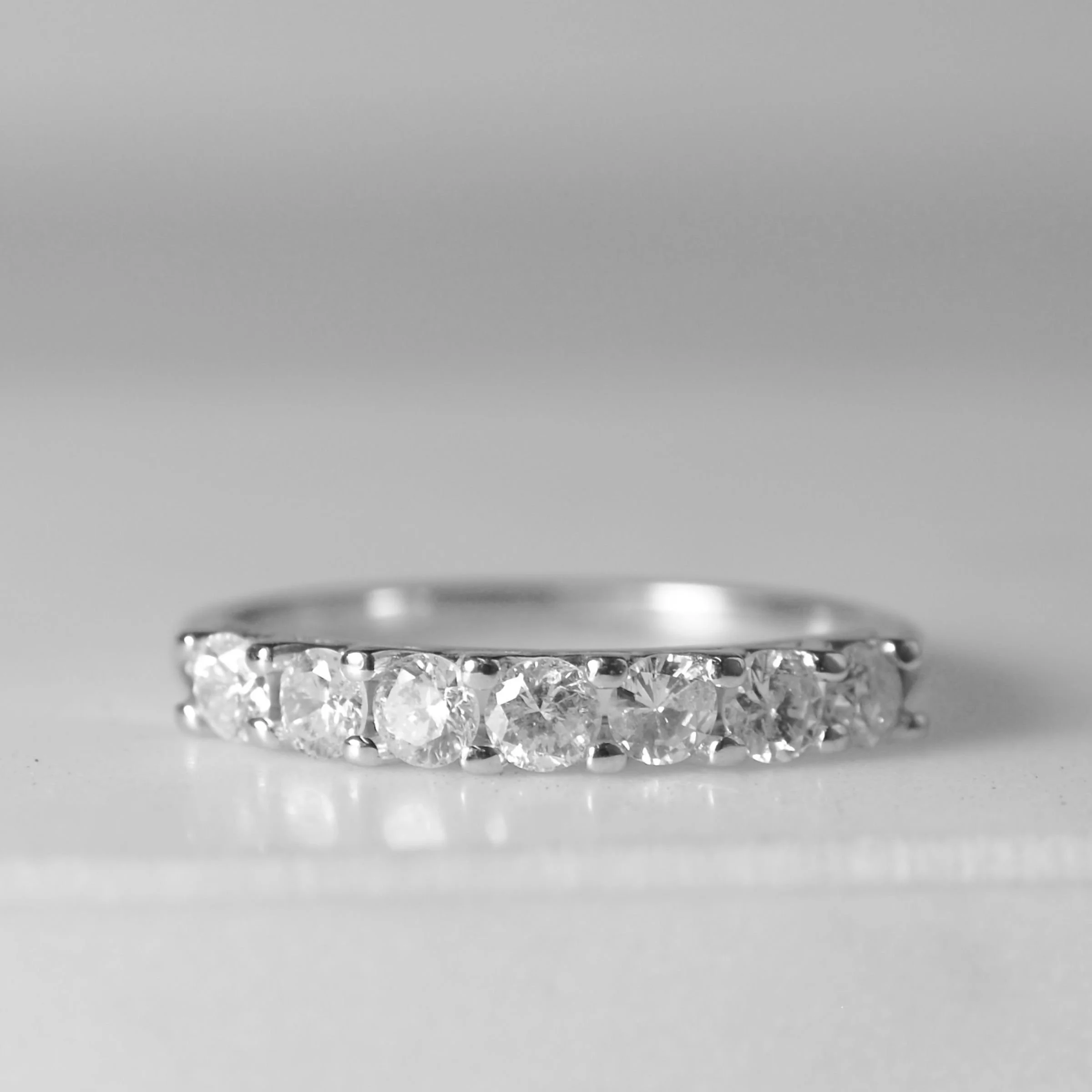 Heirloom Redesign-  A white gold seven-stone diamond anniversary ring featuring a row of shared-prong round brilliant cut diamonds set across the top band set in platinum.