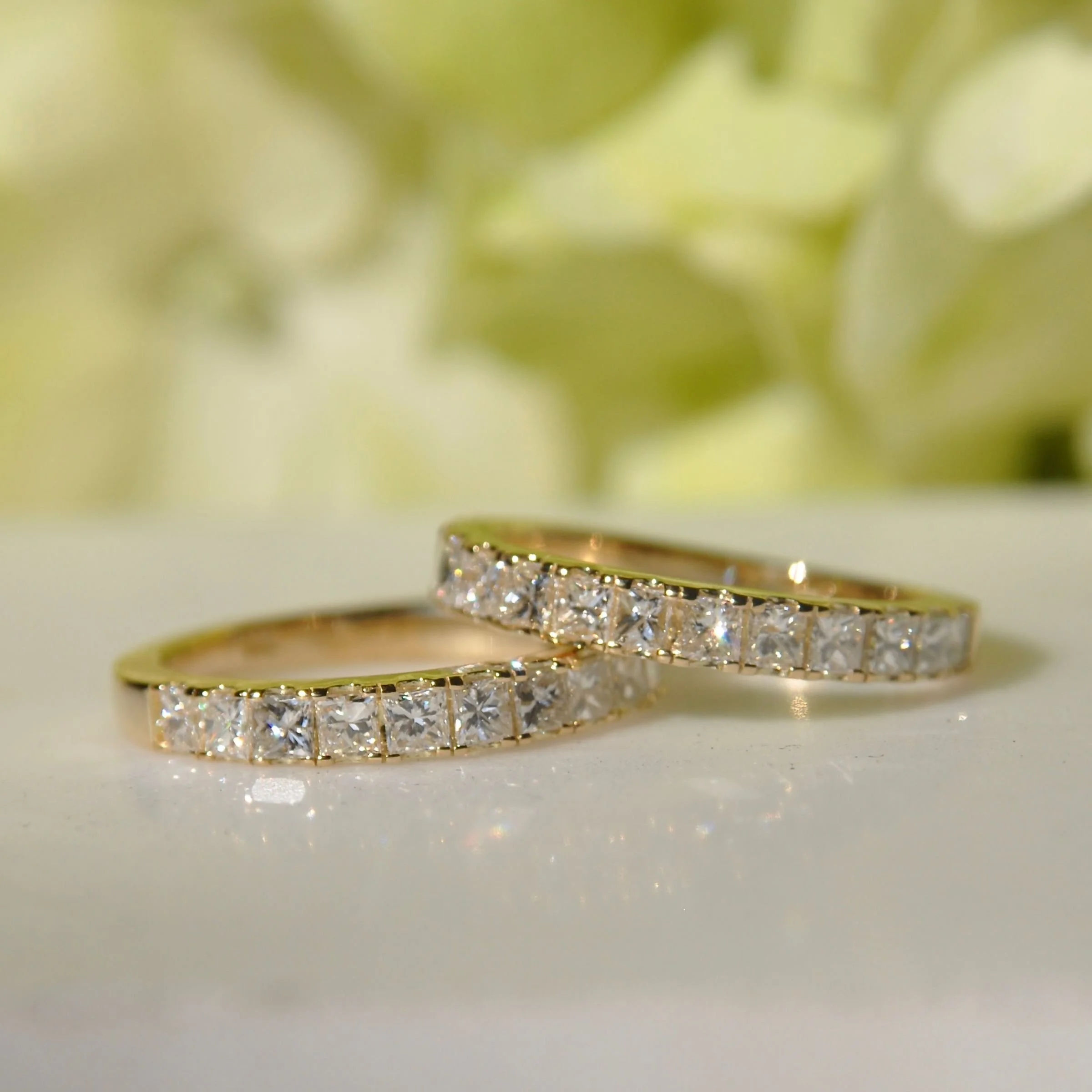 A pair of modern matching 18k yellow gold wedding rings featuring square princess-cut diamonds set in a channel-style shared-prong eternity band design