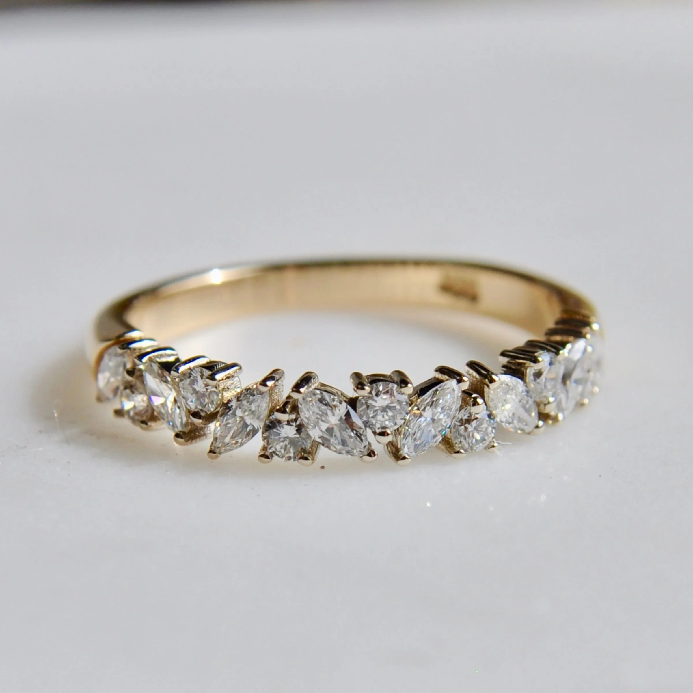 A contemporary 18k gold multi-stone wedding ring showcasing an alternating marquise and round cut diamond band with a shared prong setting on a polished gold shank